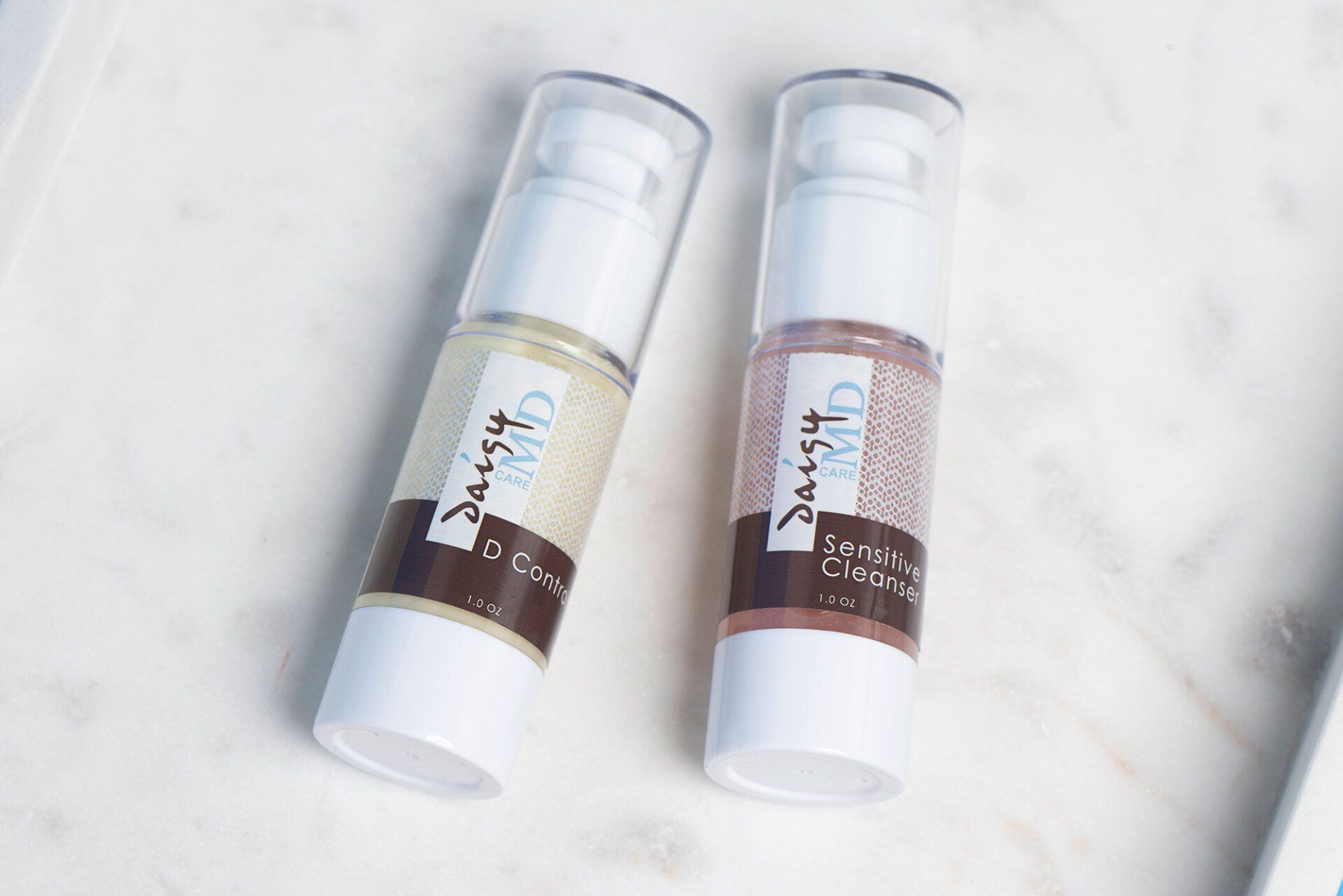 Two skincare product bottles on a white marble surface.