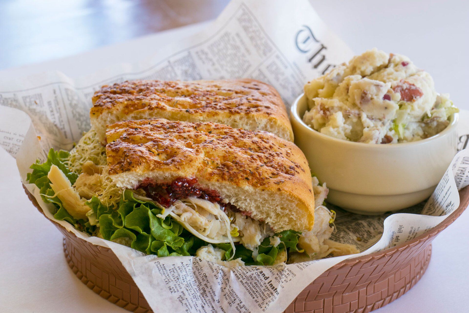 Sandwich and potato salad in a basket, on newspaper.