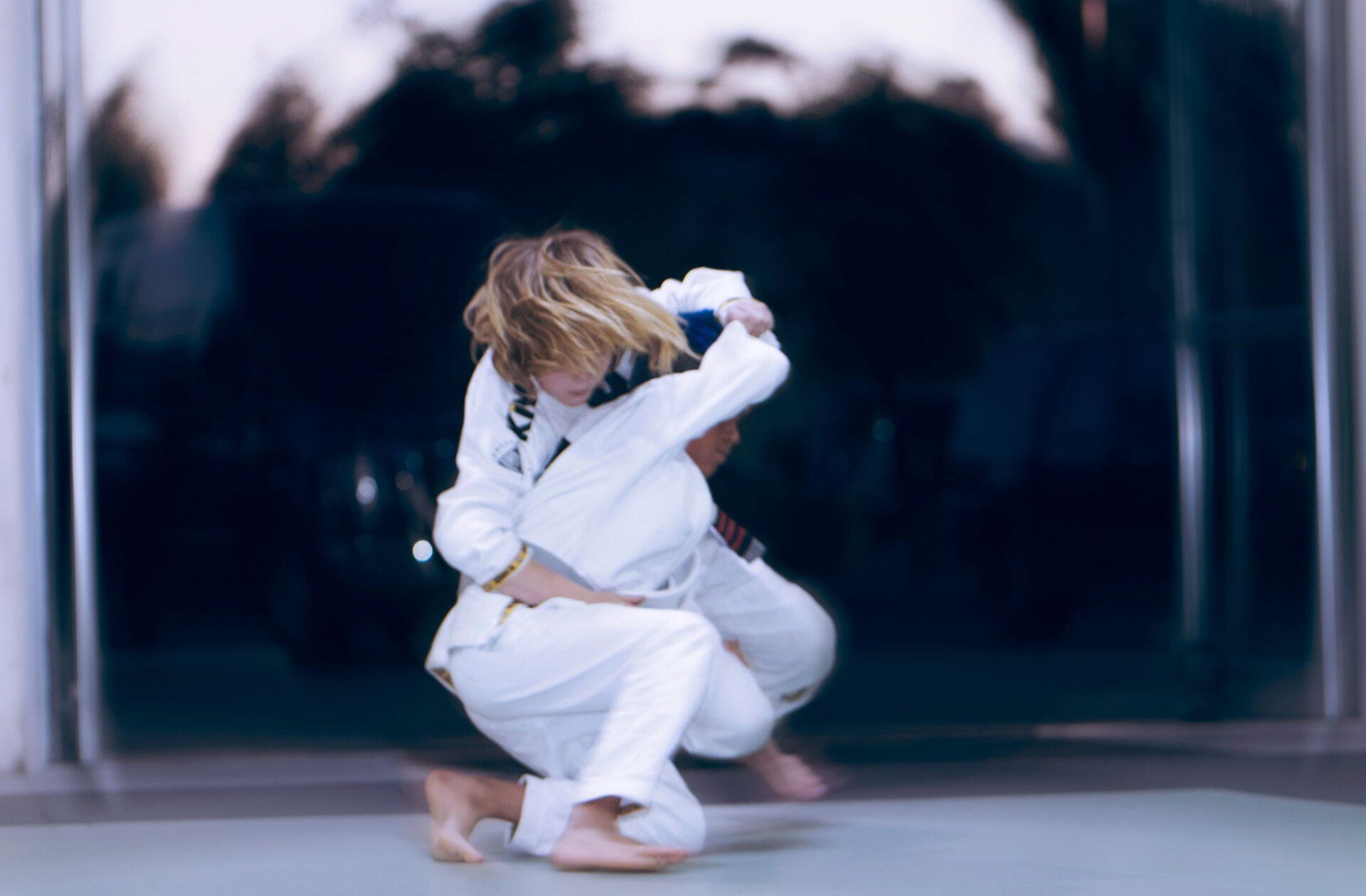 Two people in white martial arts uniforms grappling on a mat. One appears to be executing a throw.