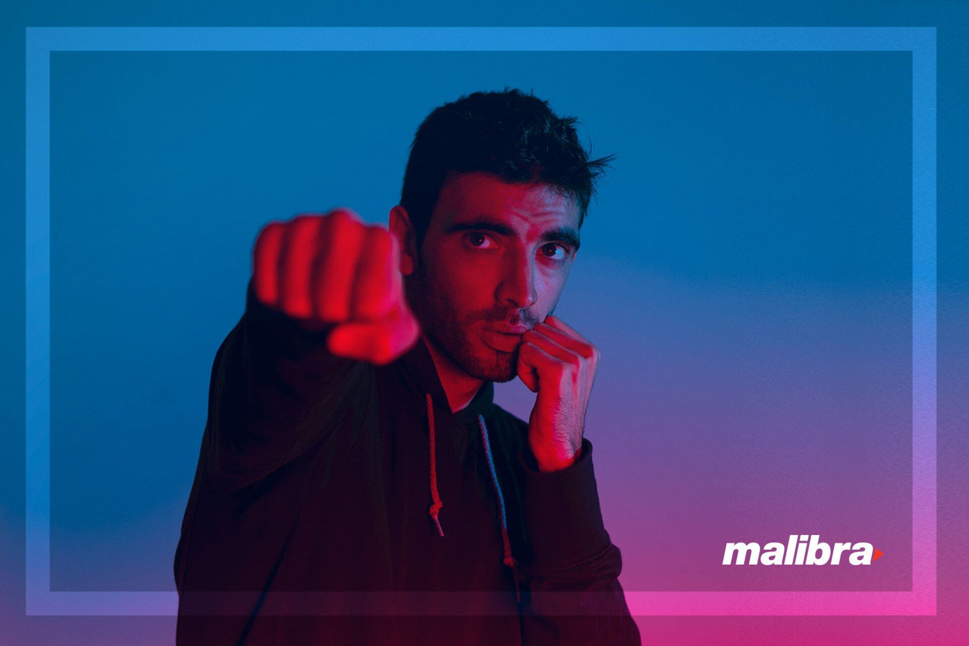 Man in black hoodie, fist raised, facing forward; blue and red gradient background,