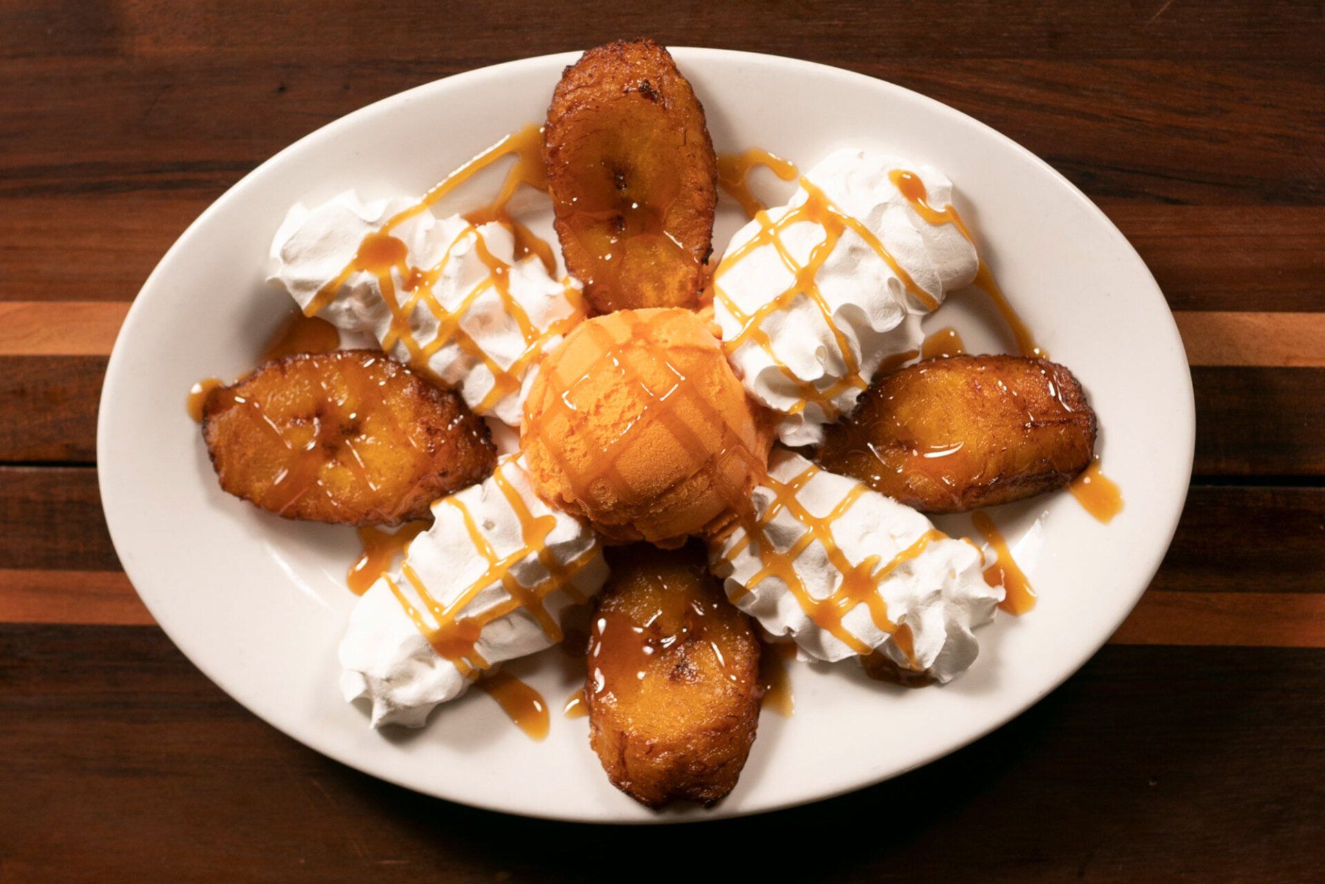 Plate of fried plantains with whipped cream and caramel drizzle.