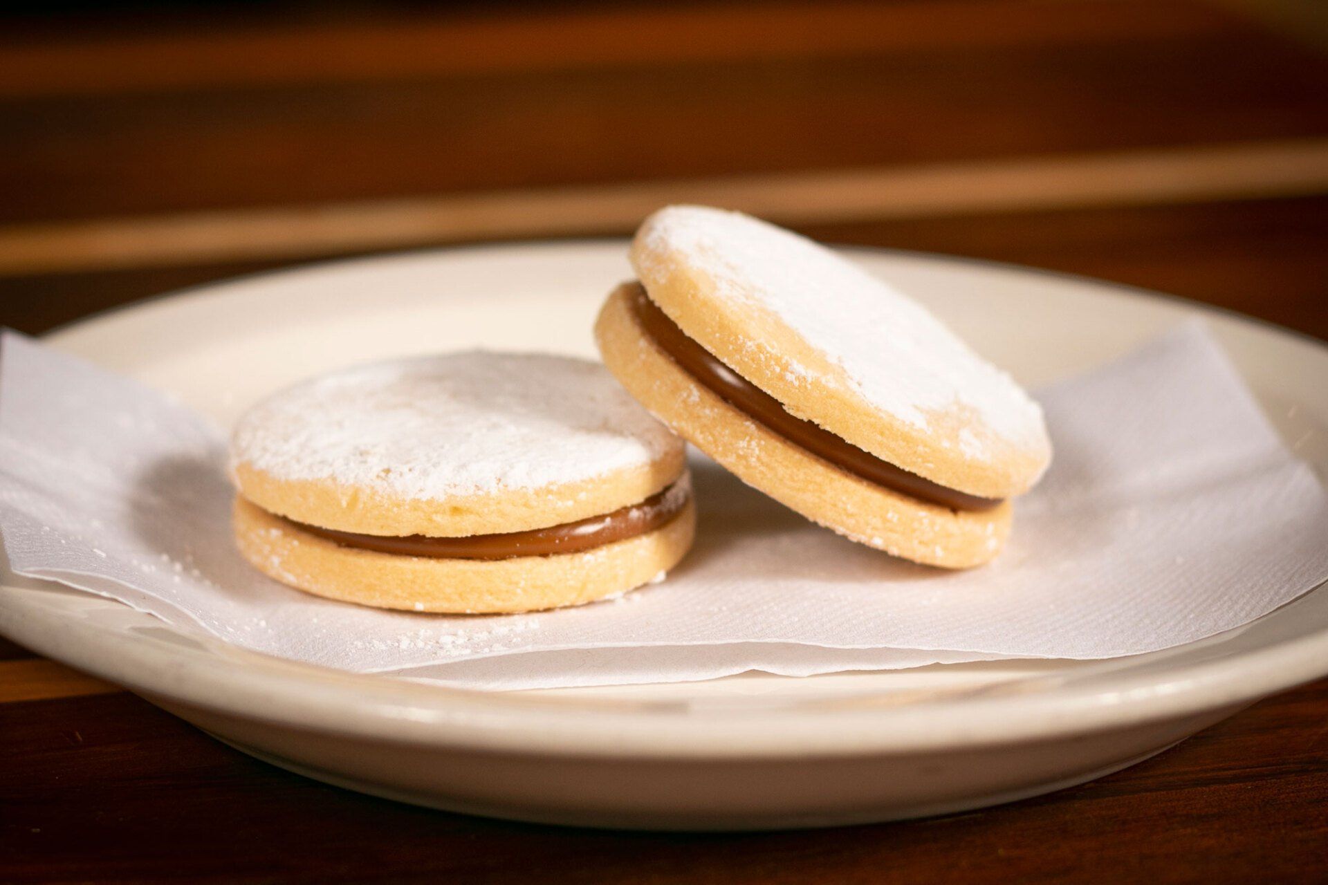 Two alfajores cookies filled with dulce de leche, dusted with powdered sugar, on a white plate.