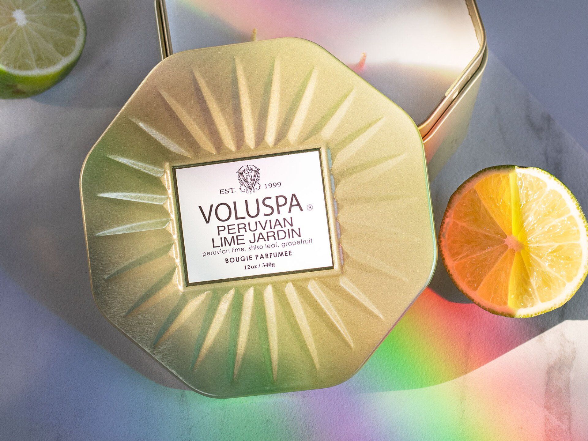 Voluspa candle in a gold and green container with halved lime, rainbow prism effect.