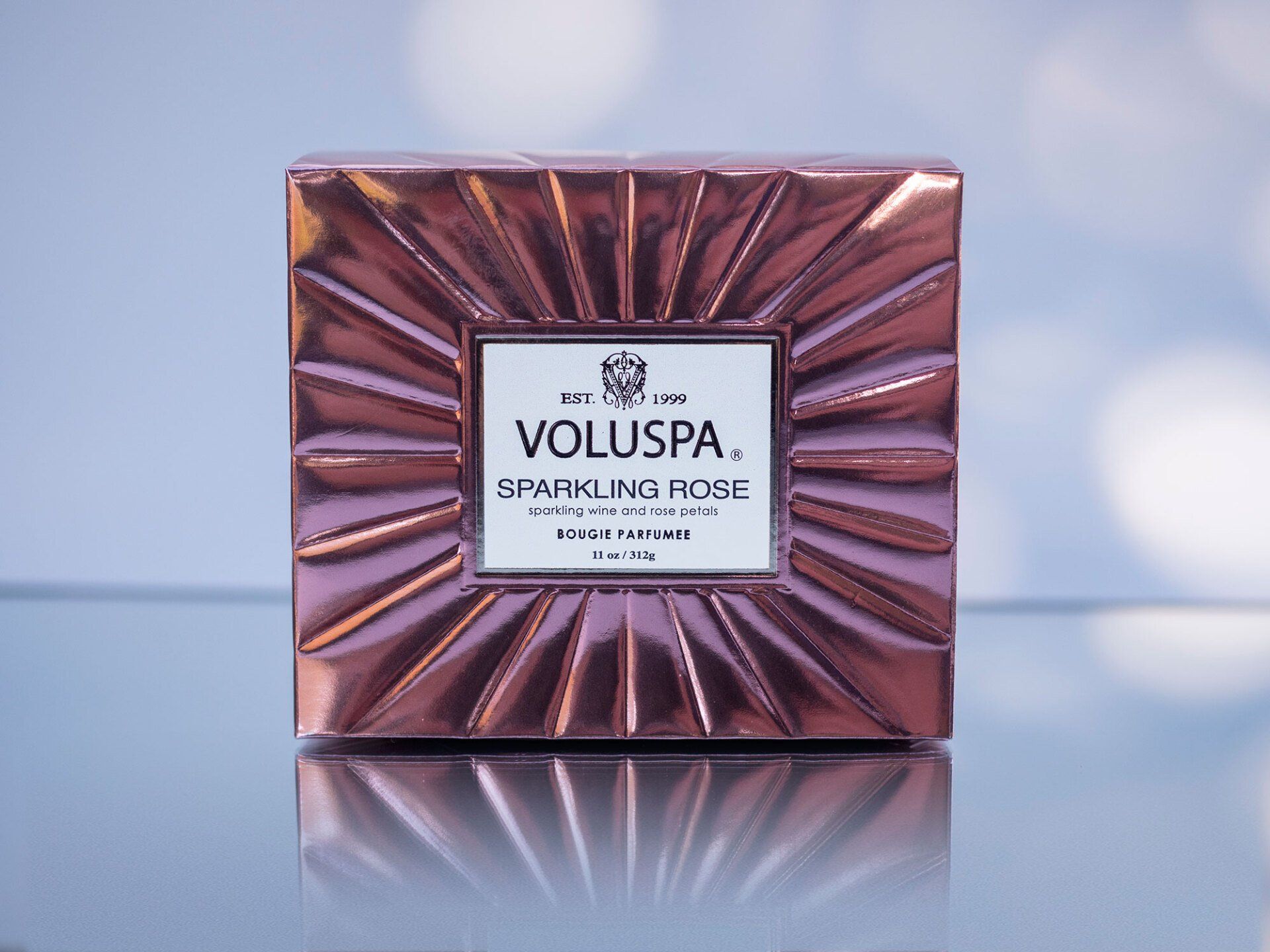 Square, metallic pink Voluspa candle box with a white label reading 