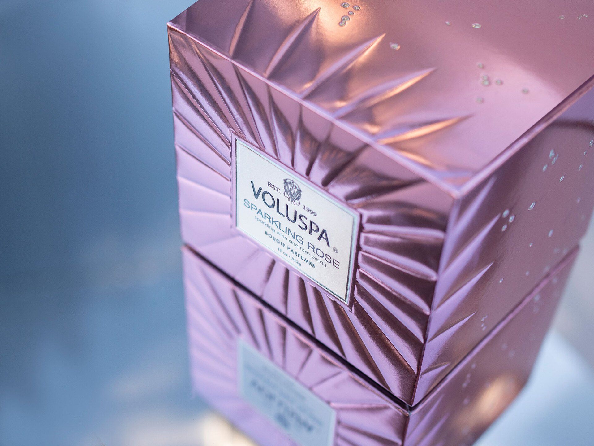 Pink, textured Voluspa candle boxes stacked. Label reads 