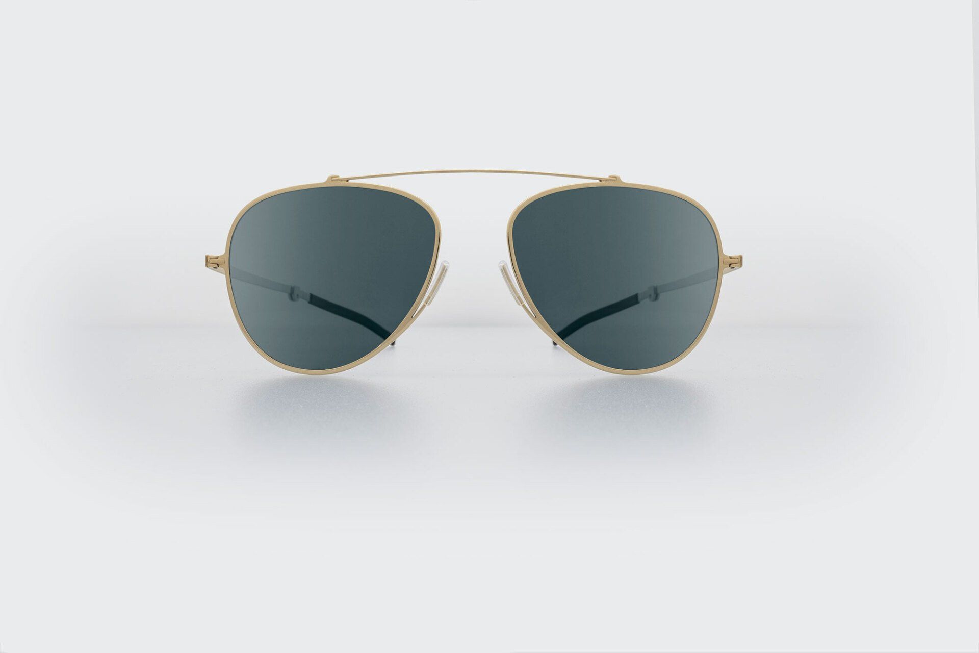 Gold-framed aviator sunglasses with dark lenses, resting on a white surface.