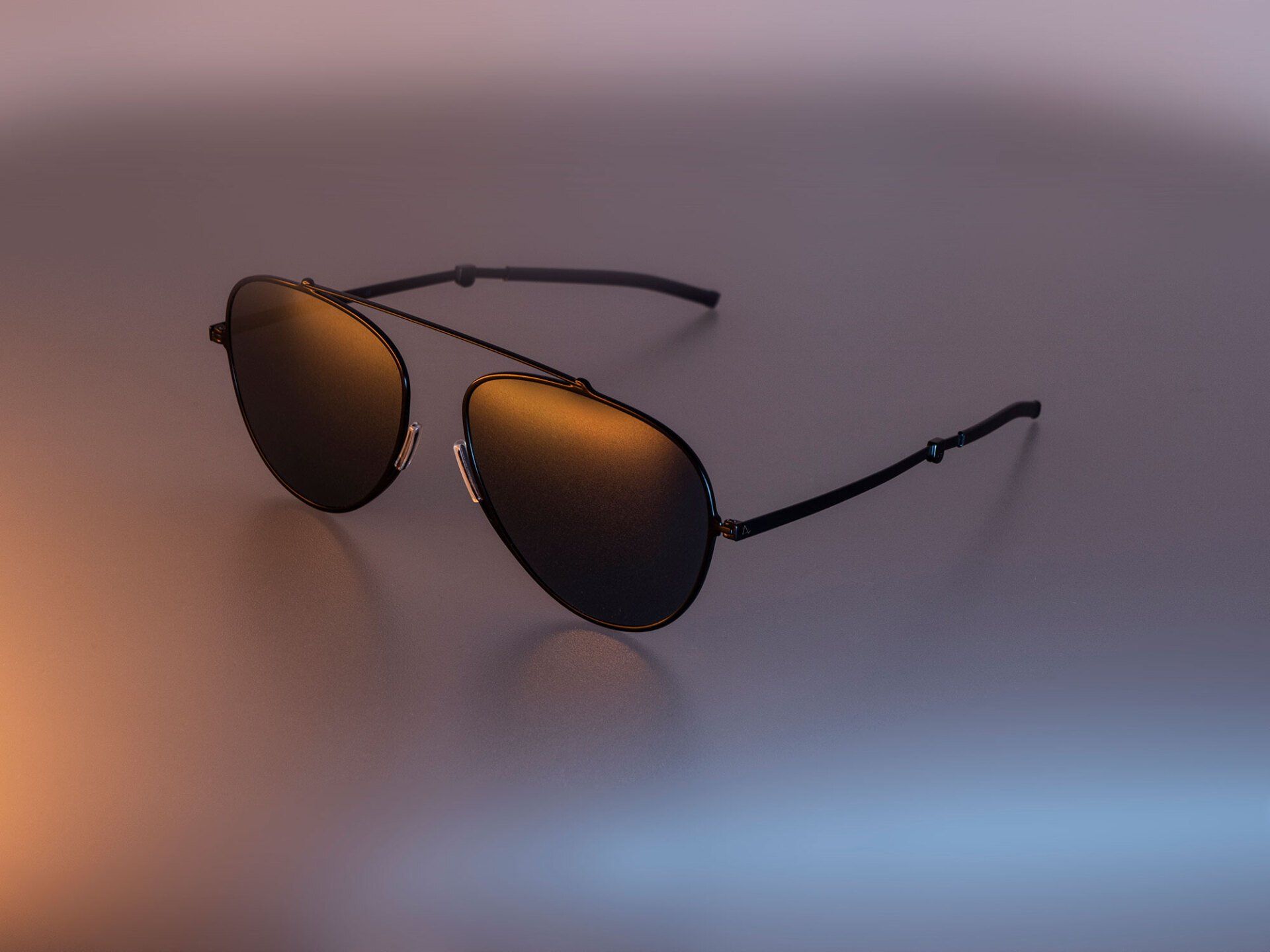 Black aviator sunglasses on a reflective surface with orange and blue lighting.