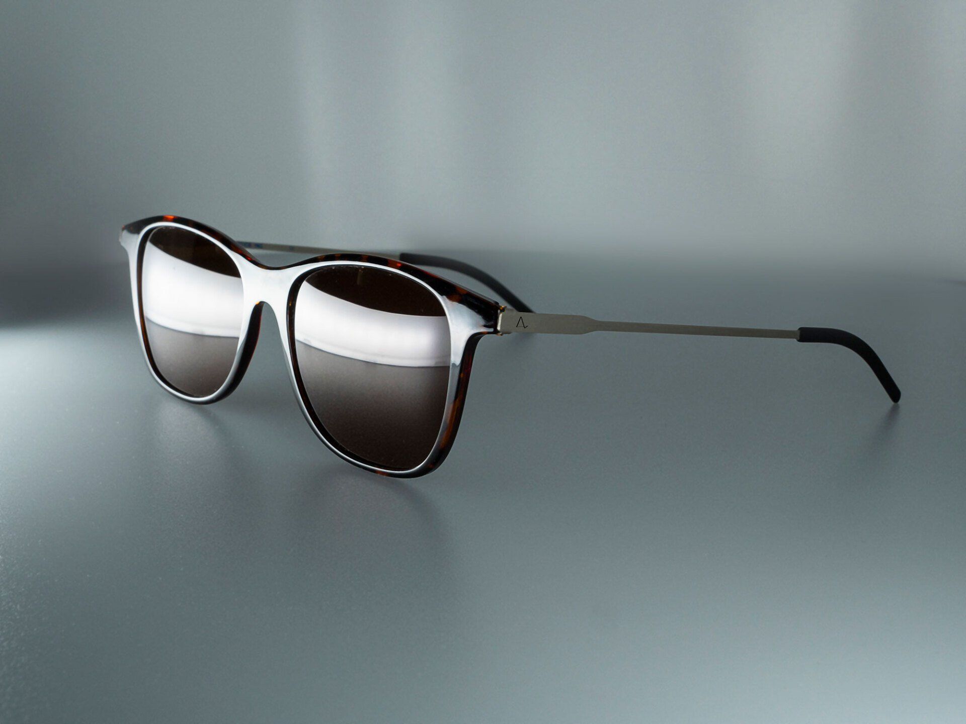 Sunglasses with brown lenses and silver frames resting on a reflective surface.