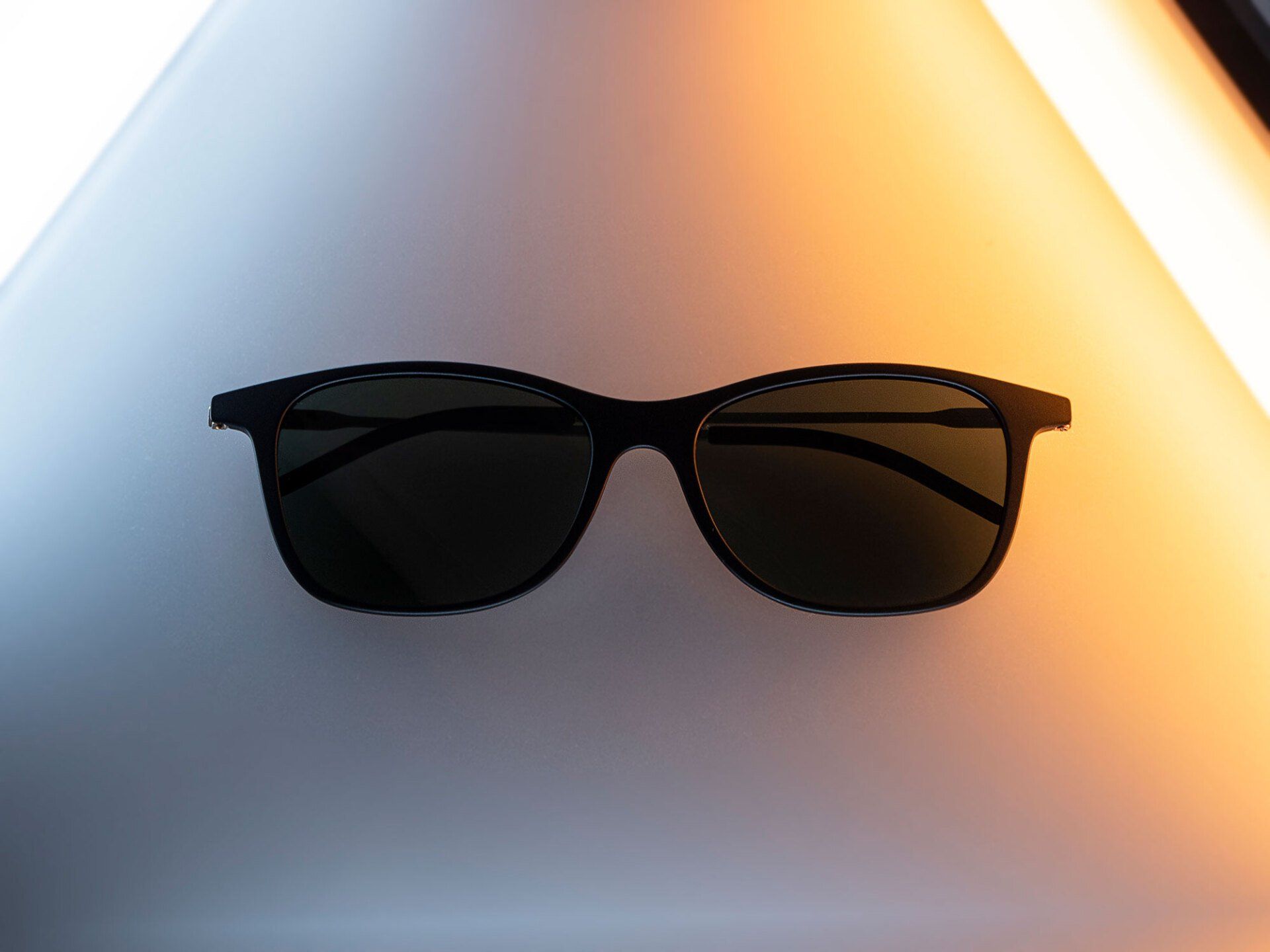Black sunglasses on a white and orange gradient background.