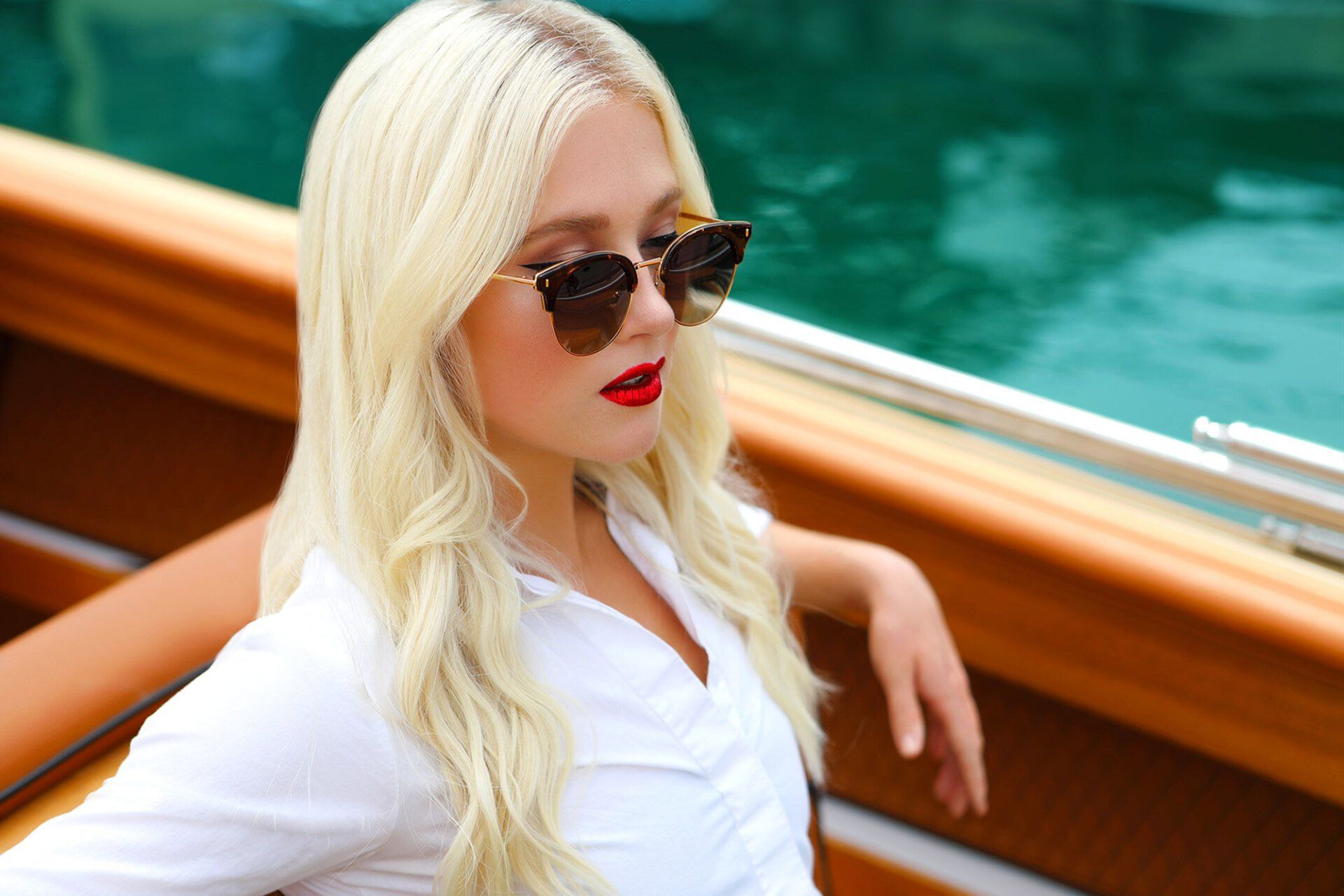 Woman in sunglasses and white shirt on a boat with turquoise water background.