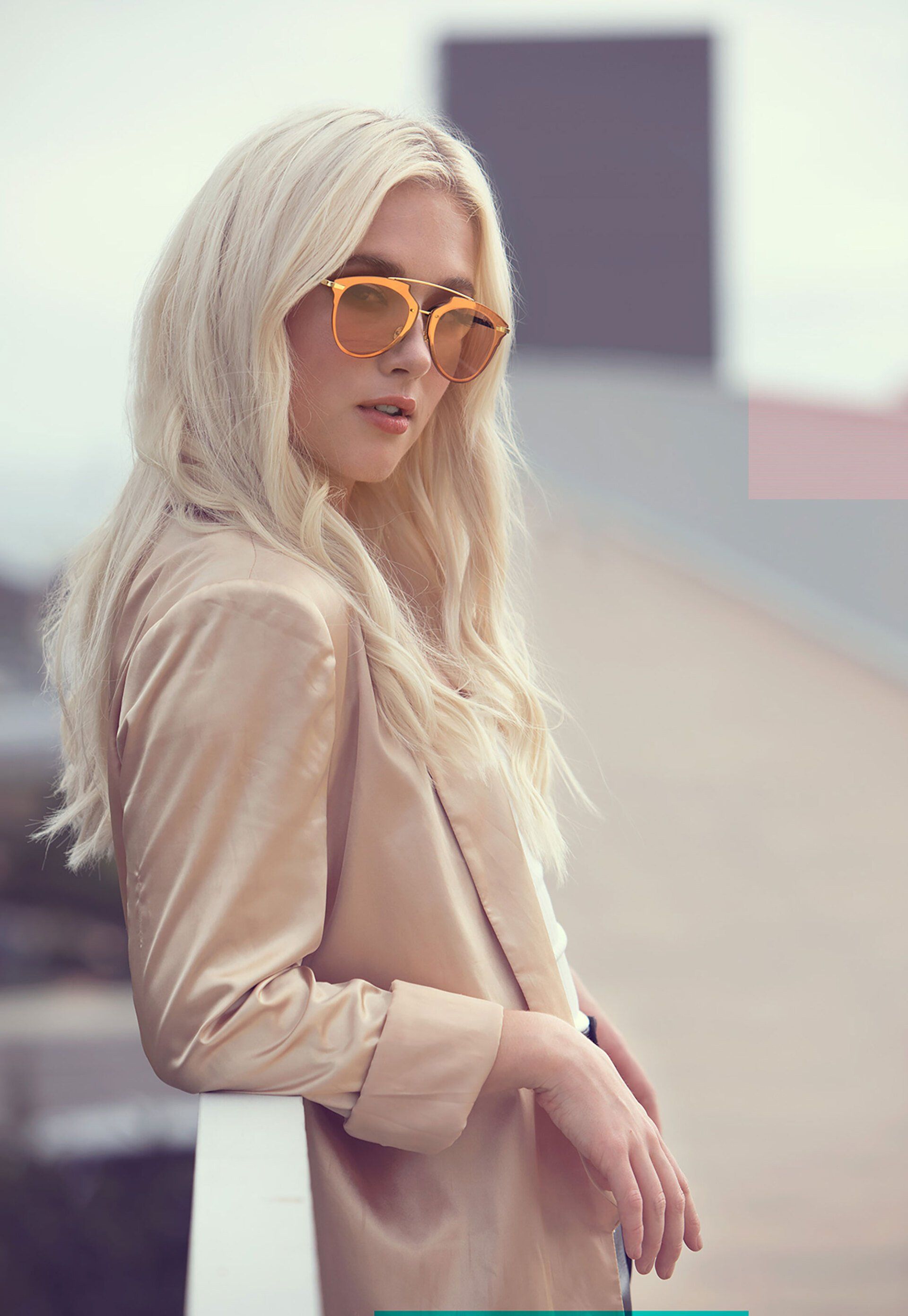Blonde person in tan blazer and orange sunglasses, leaning on a white railing.