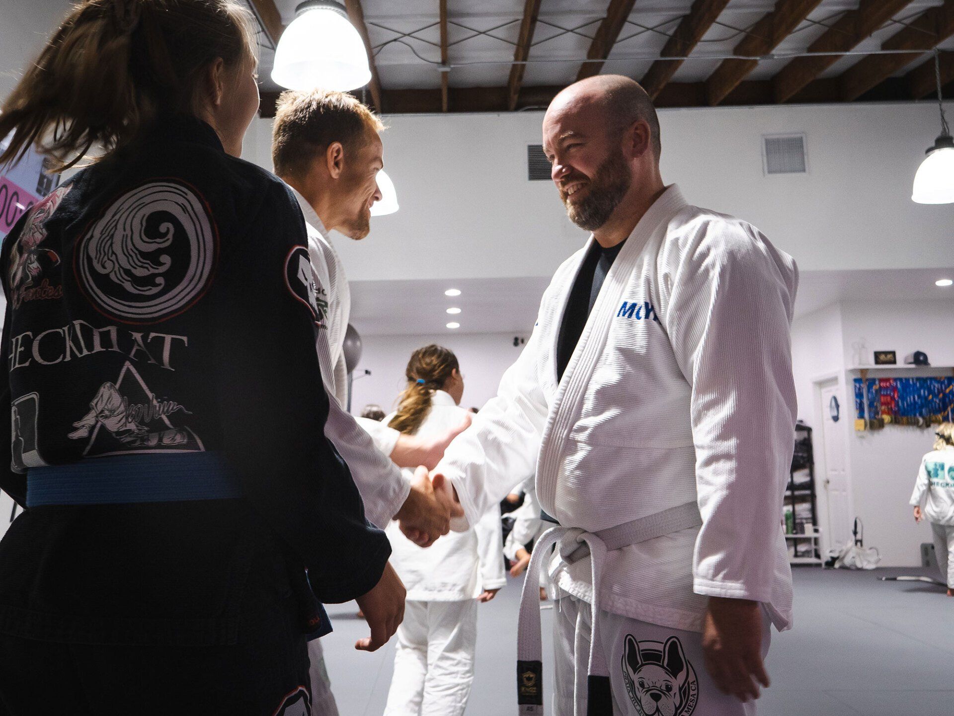 Martial arts students shaking hands in a gym, wearing white and blue gis.