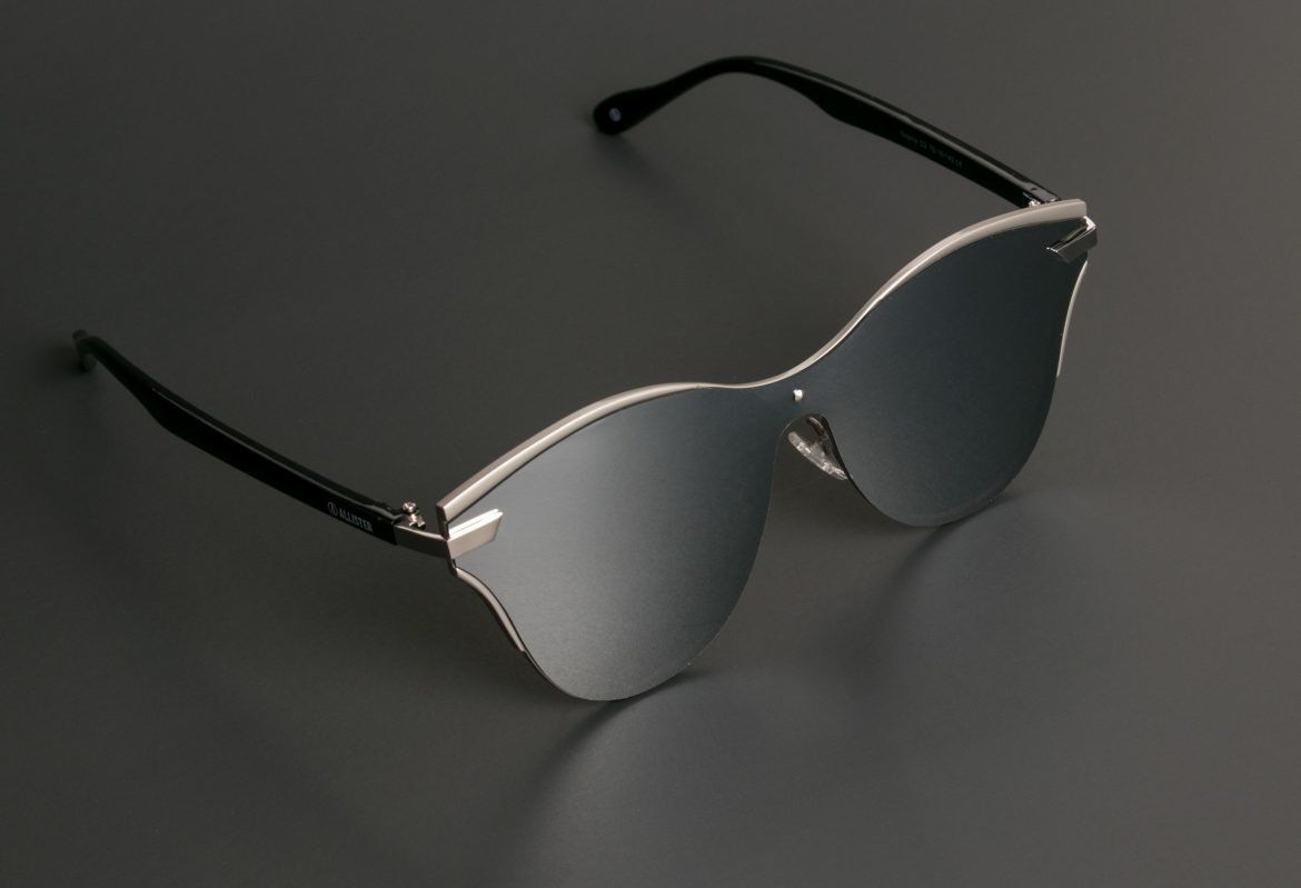 Silver mirrored sunglasses with black arms on a gray surface.