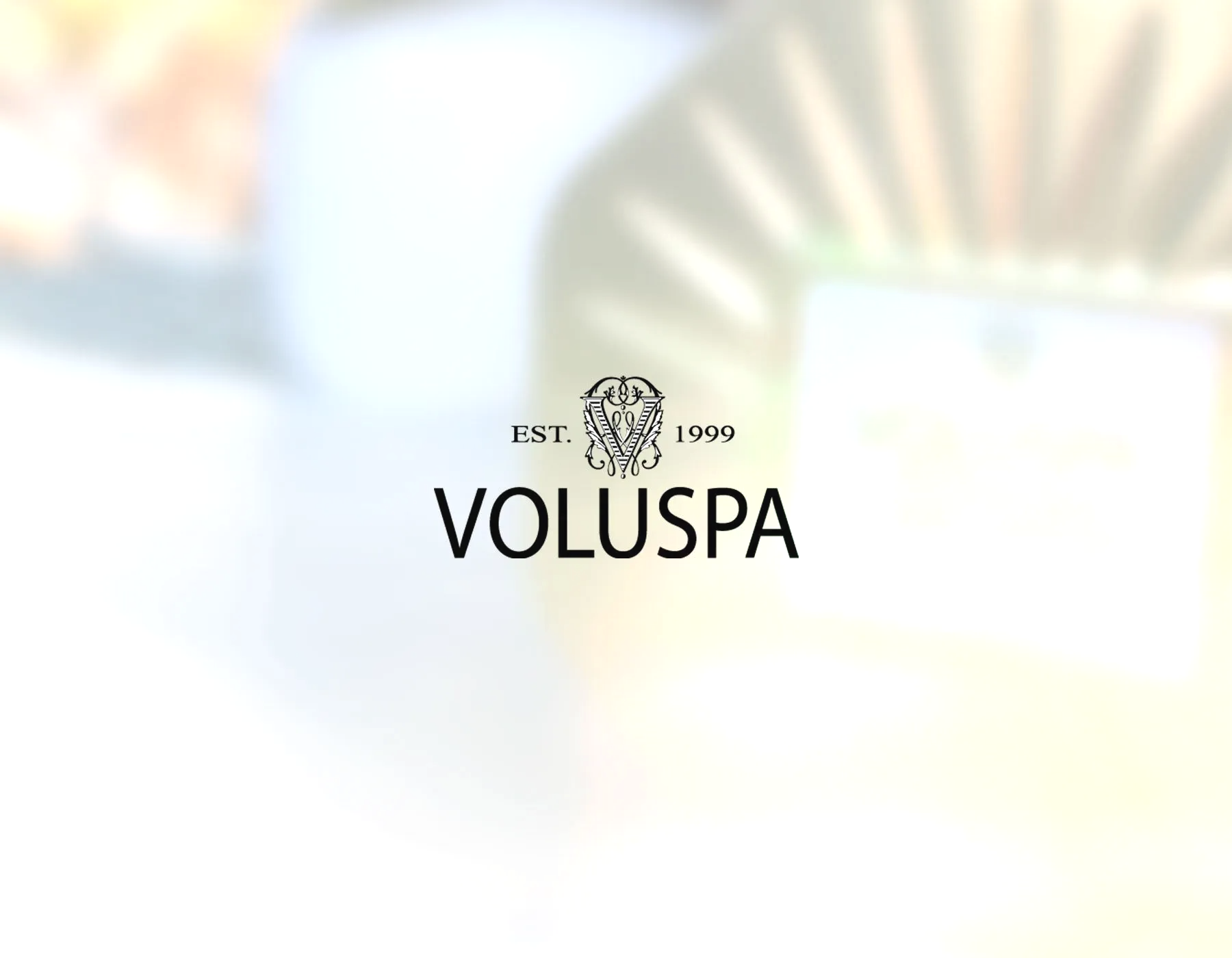 Voluspa logo with a blurry background of a candle or similar product.