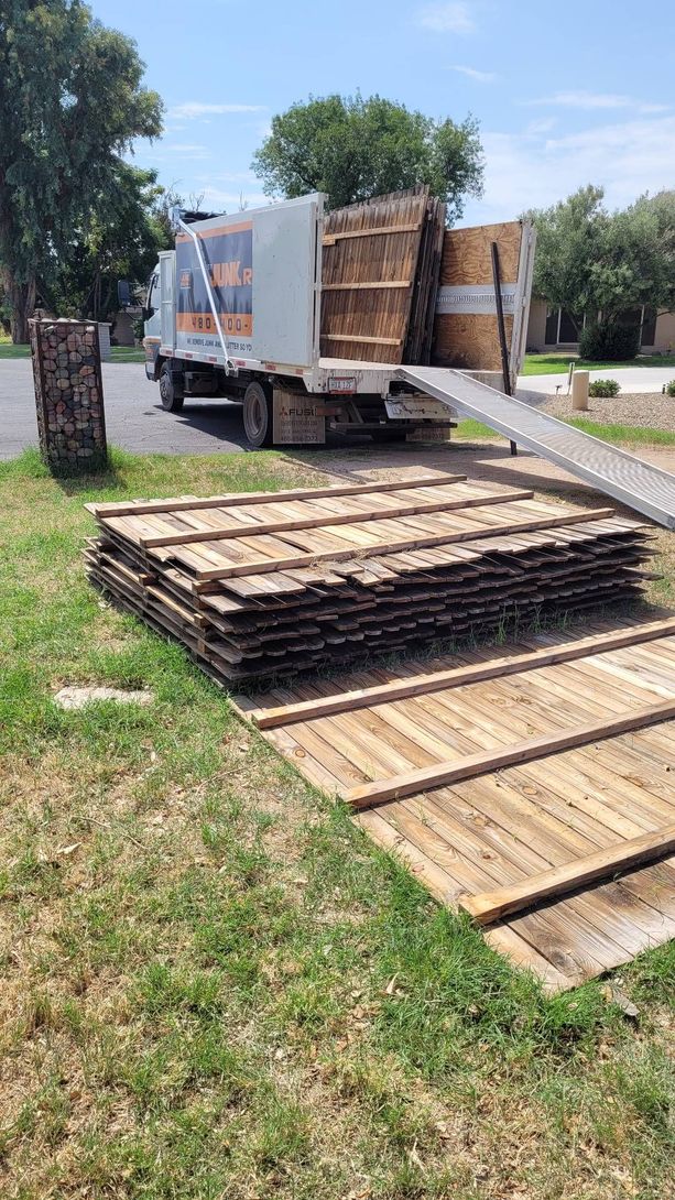 Truck unloading wooden pallets onto grass near a sidewalk on a sunny day