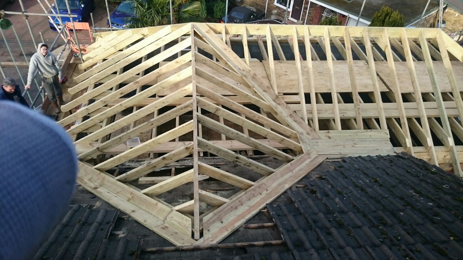 A partially constructed wooden roof frame with rafters and a hip section, showing construction progress on a home exterior.