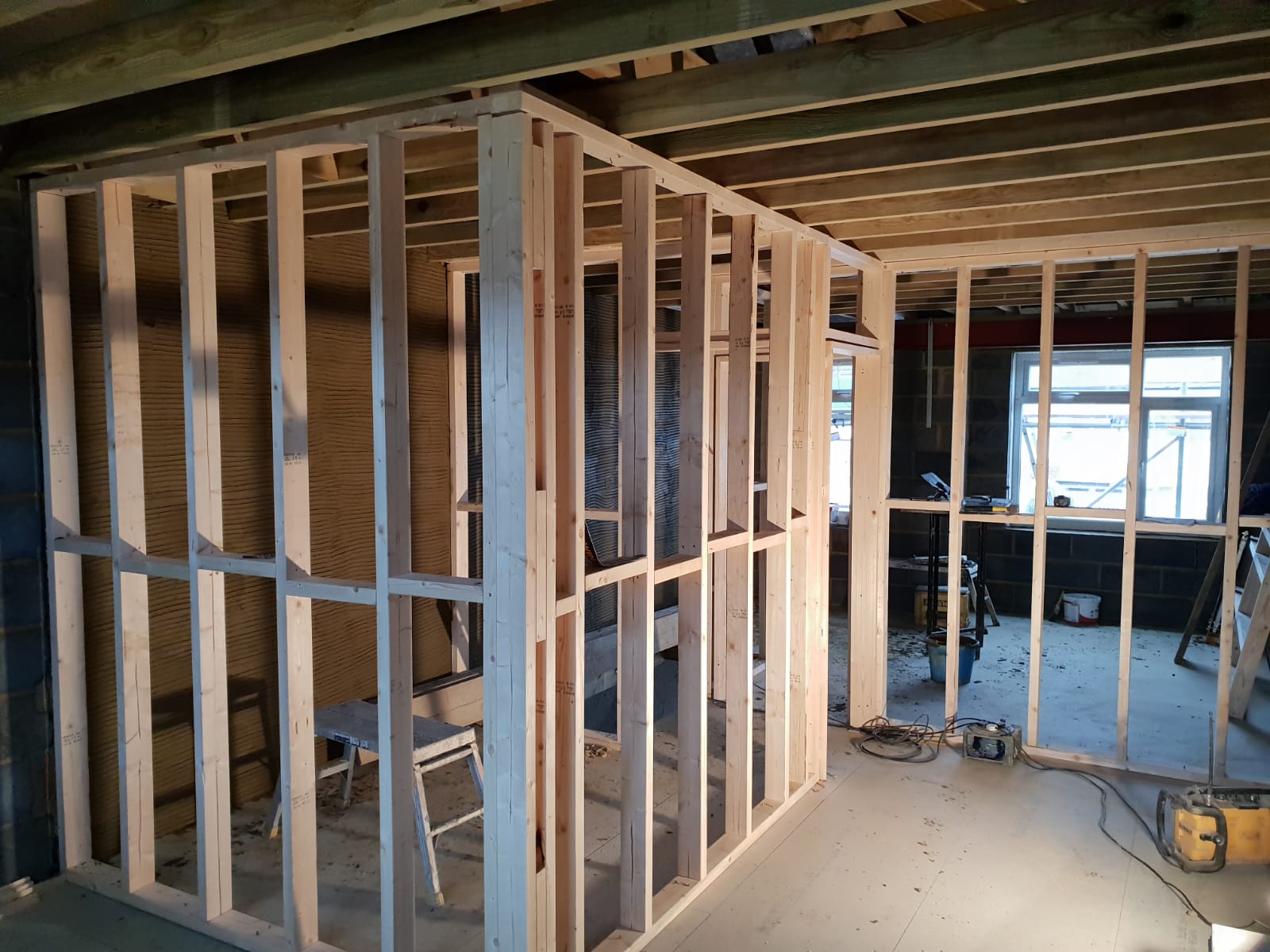 Unfinished wooden wall framing for a room under construction inside a building with visible joists and floor.