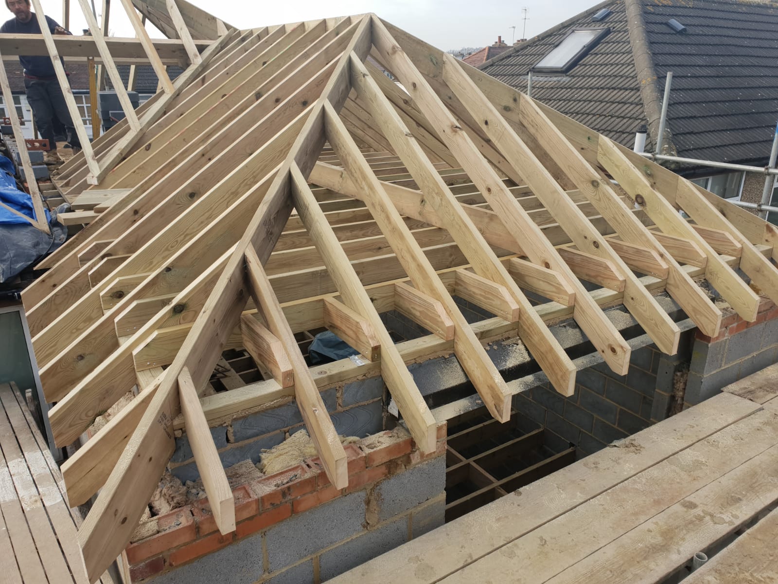 Hillrose House Extension Specialists Construction workers installing wooden roof rafters on a building structure under a gray sky.