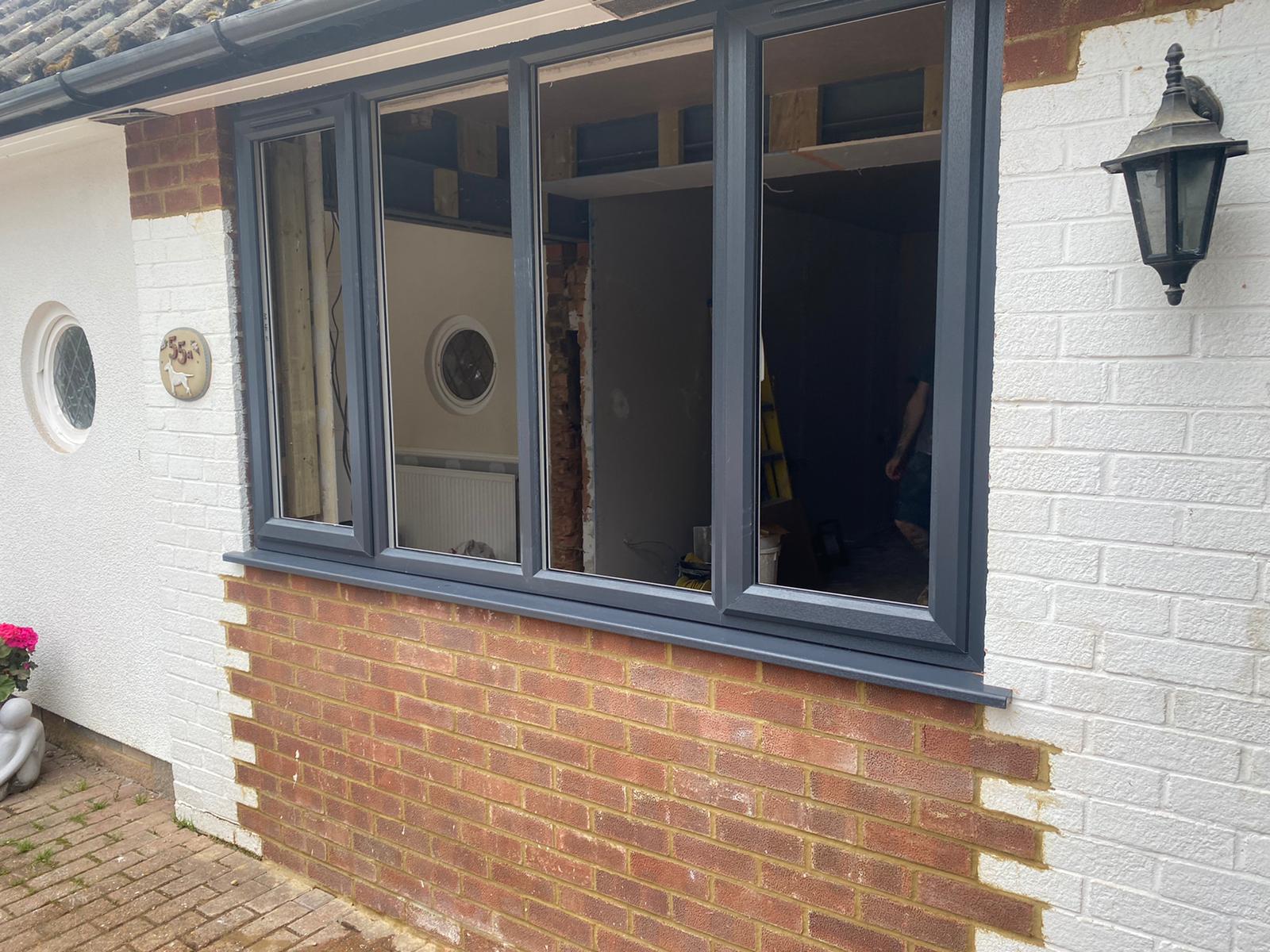 Garage Conversions A dark gray window frame installed in a white-painted brick house wall with an exposed brick section beneath the window.
