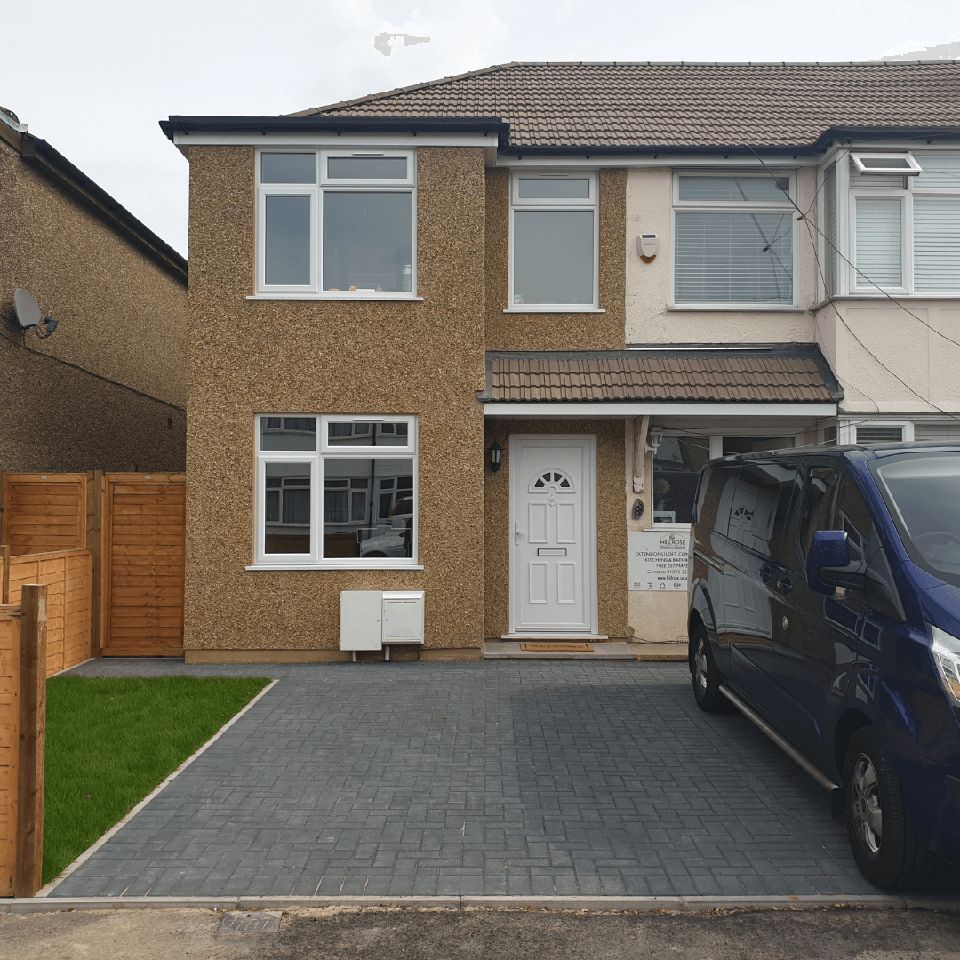A two-story semi-detached house with a pebbledash exterior, a paved driveway, a white front door, and a small grass patch.