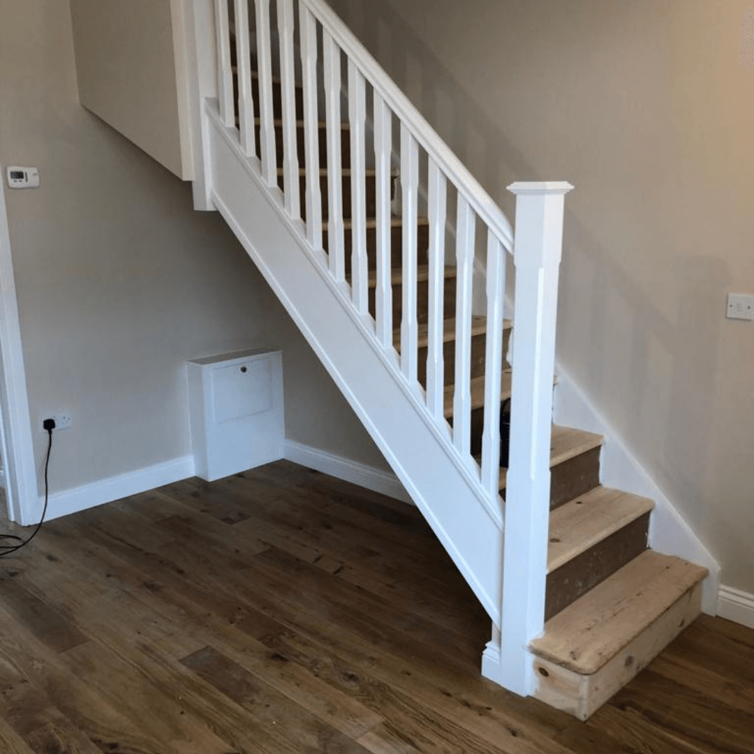 A staircase with white railings and natural wooden treads positioned over a wooden floor in a home interior.