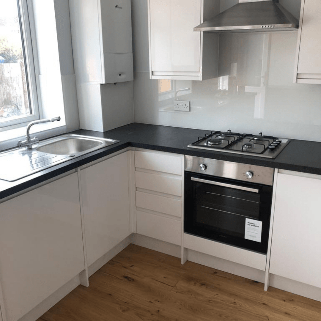 Modern kitchen with white cabinets, dark countertop, stainless steel oven, gas hob, and a sink by a window.
