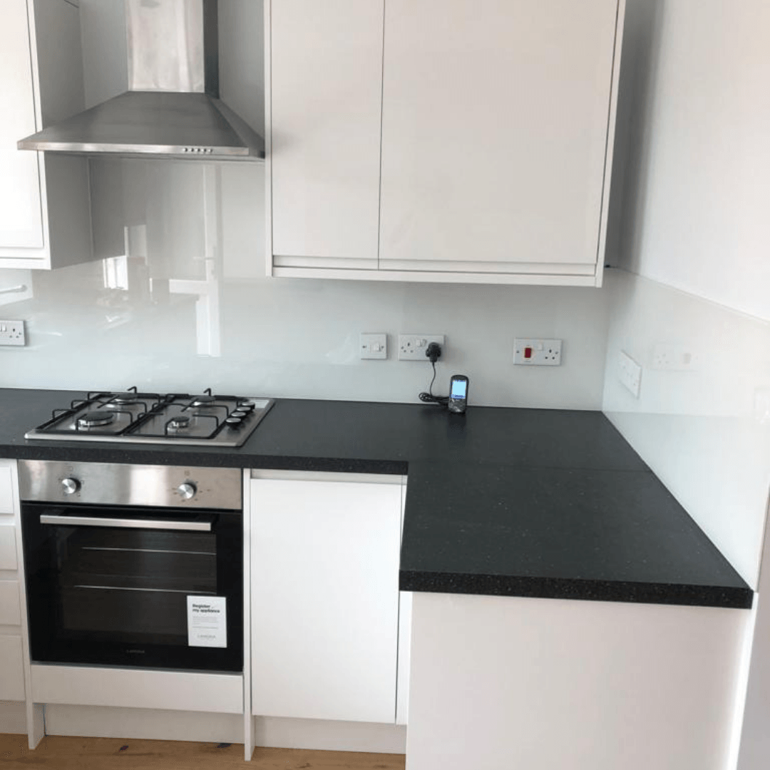 Modern kitchen featuring a stainless steel oven and gas stove, white cabinets, and a black countertop with white splashback.