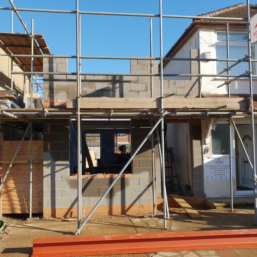 A house under construction with scaffolding surrounding an unfinished brick room extension in the backyard.