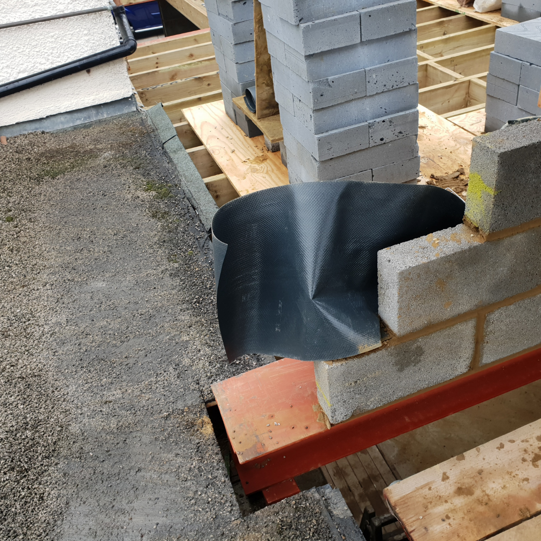 Construction site showing a piece of black damp-proof membrane placed at the corner of a new concrete block wall.