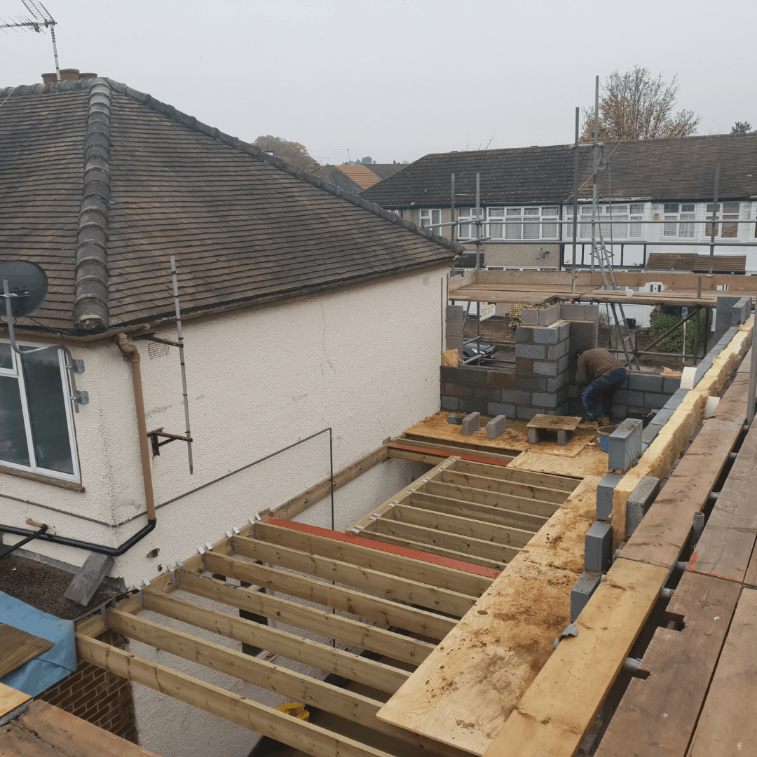 An elevated view of a residential construction site showing a house extension frame with timber joists and block walls.
