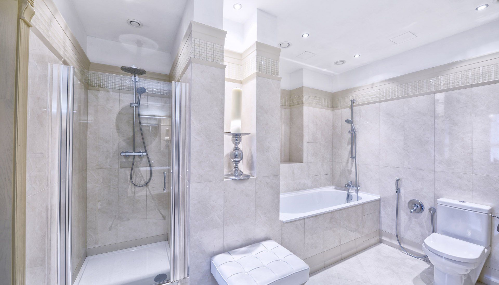 A spacious, modern bathroom with beige marble tile, a glass shower stall, a soaking bathtub, and a white toilet.