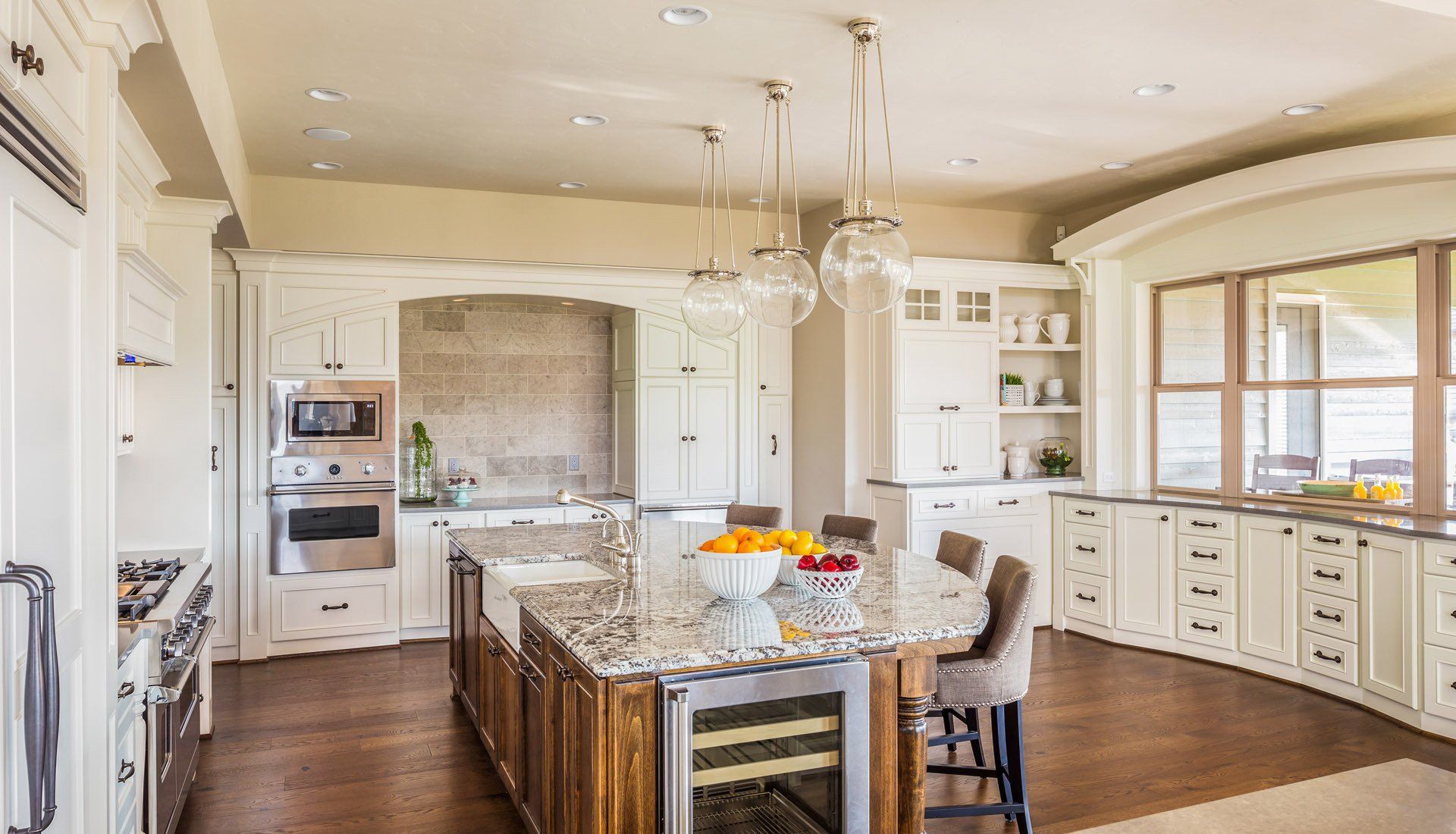 A spacious, white-themed luxury kitchen featuring a large wooden island with granite countertops and hanging glass lights.