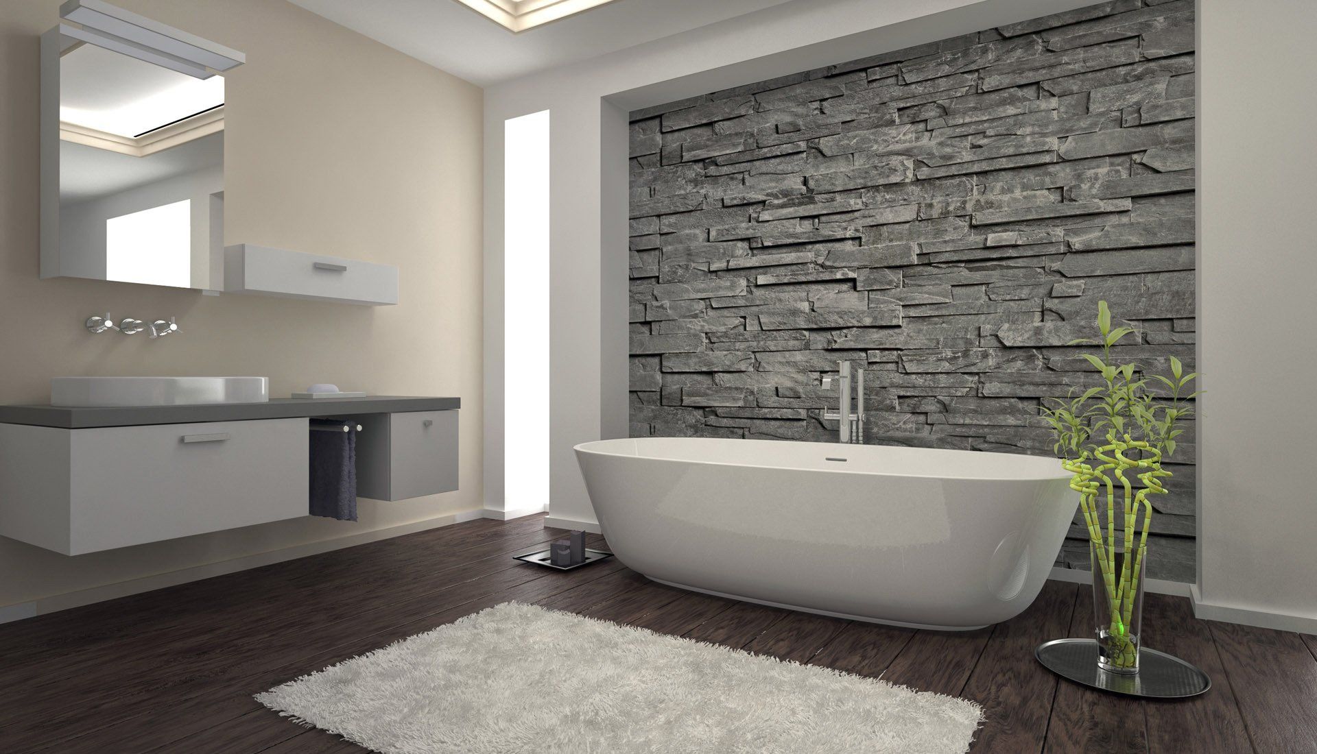 Modern bathroom with a freestanding white tub against a gray stone feature wall, dark wood floors, and vanity.