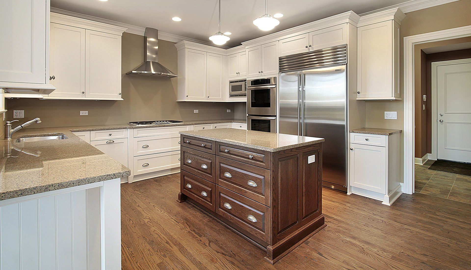 A kitchen with white cabinets, a large dark wood island, stainless steel appliances, and beige walls.