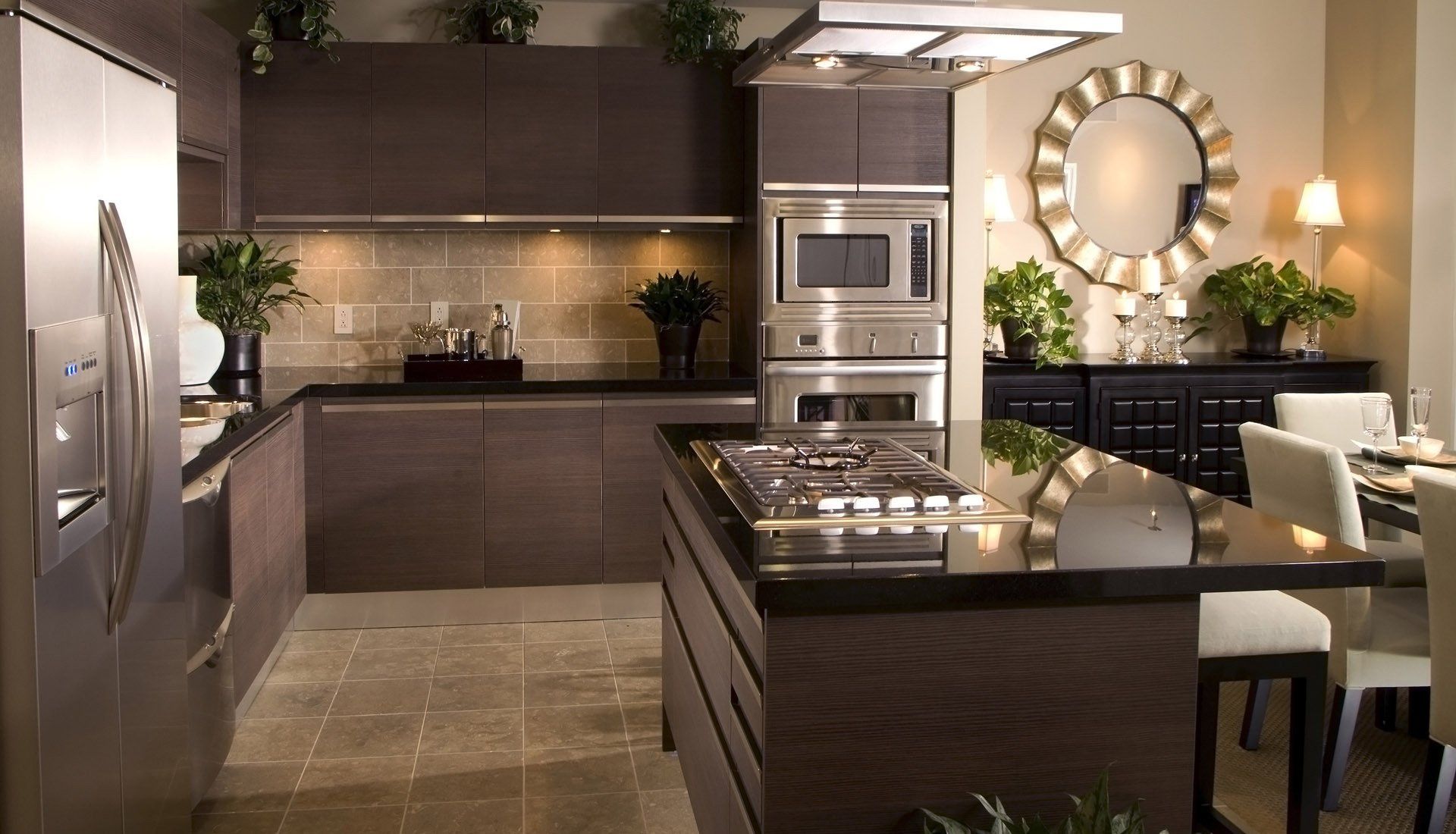 A modern kitchen with dark cabinetry, stainless steel appliances, a black granite island, and a dining area with a mirror.