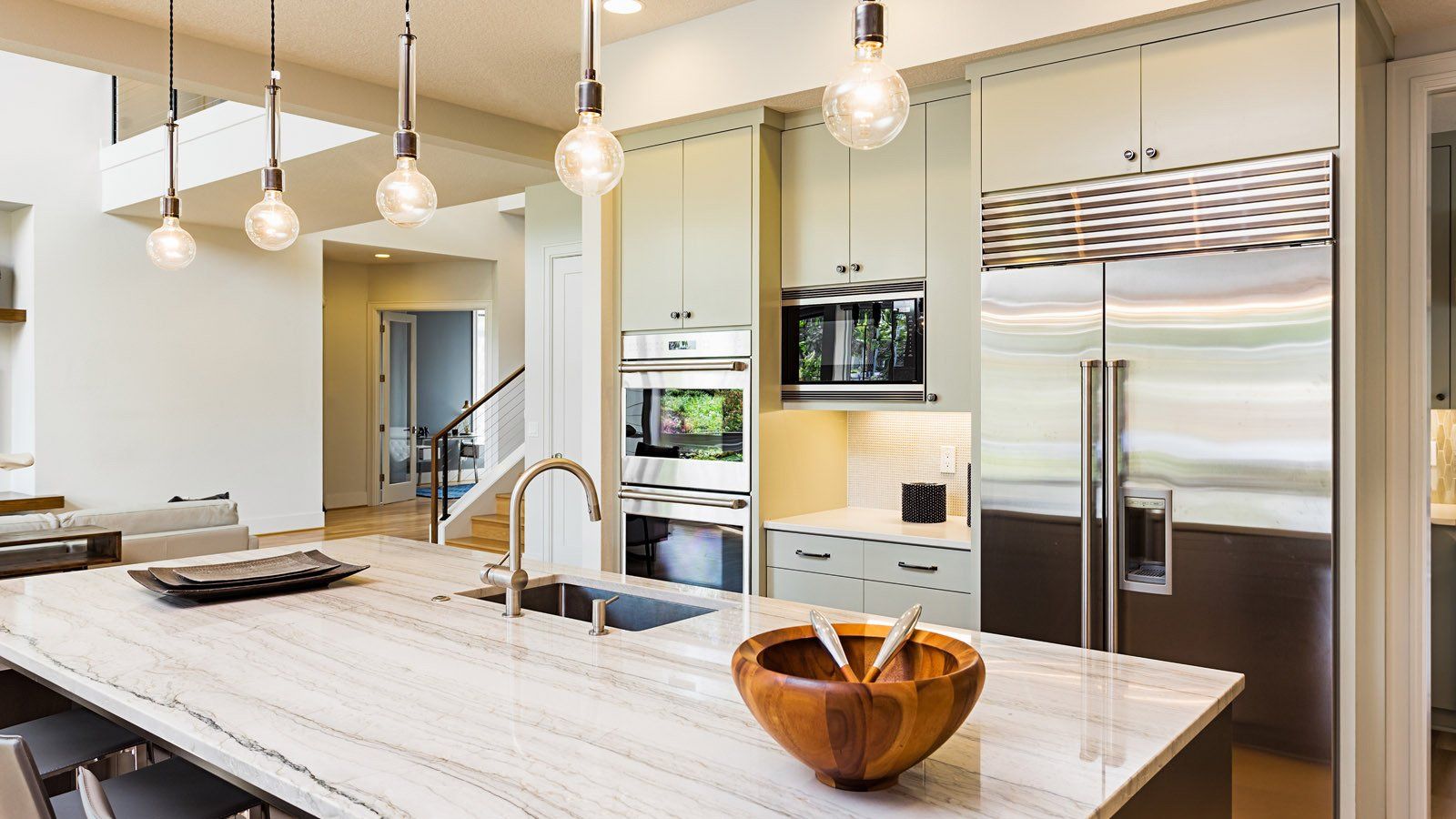 A modern kitchen with a large marble island, stainless steel appliances, and four pendant lights over the counter.