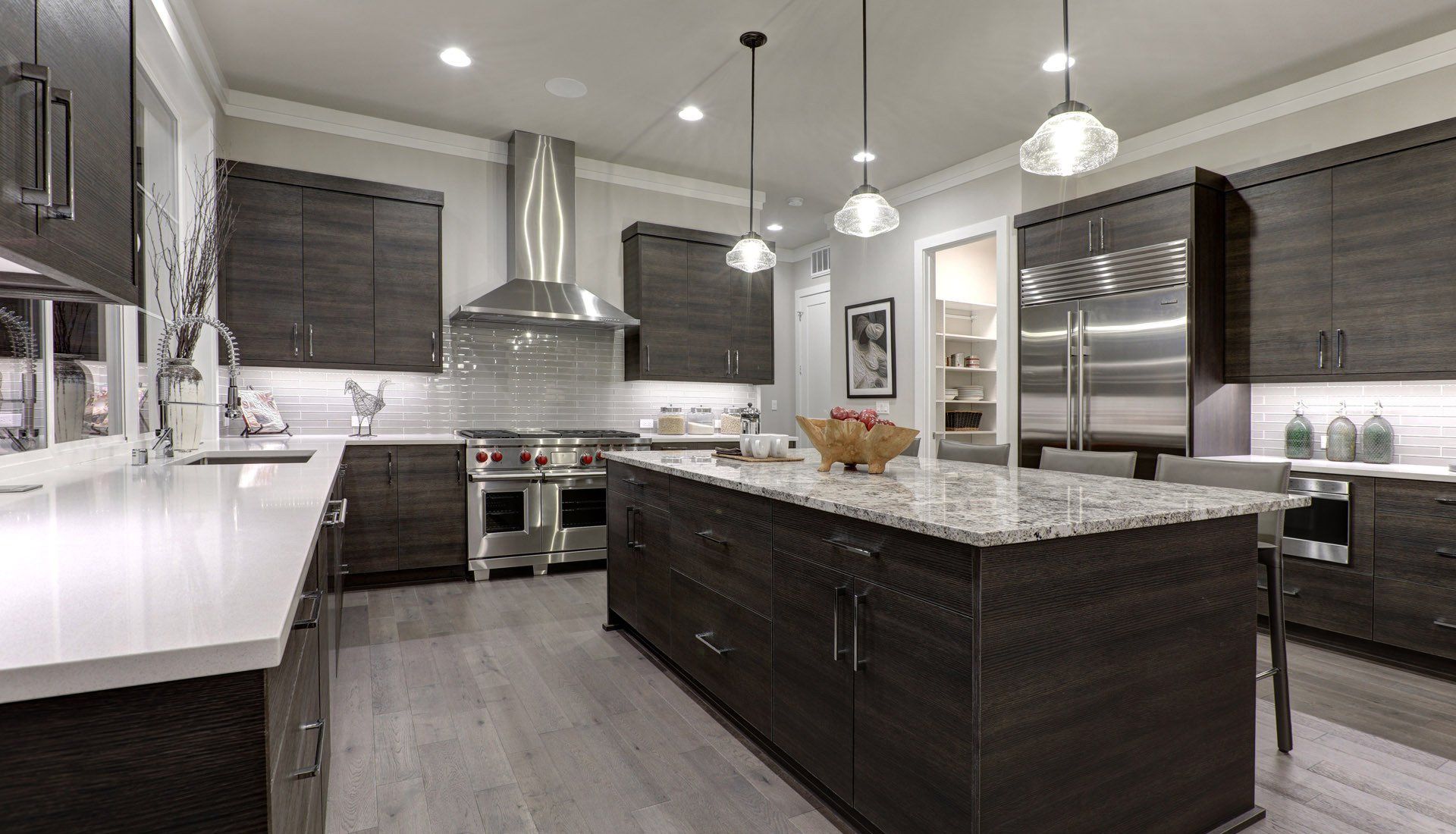 A modern kitchen features dark wood cabinets, a large granite-topped island, stainless steel appliances, and wood flooring.