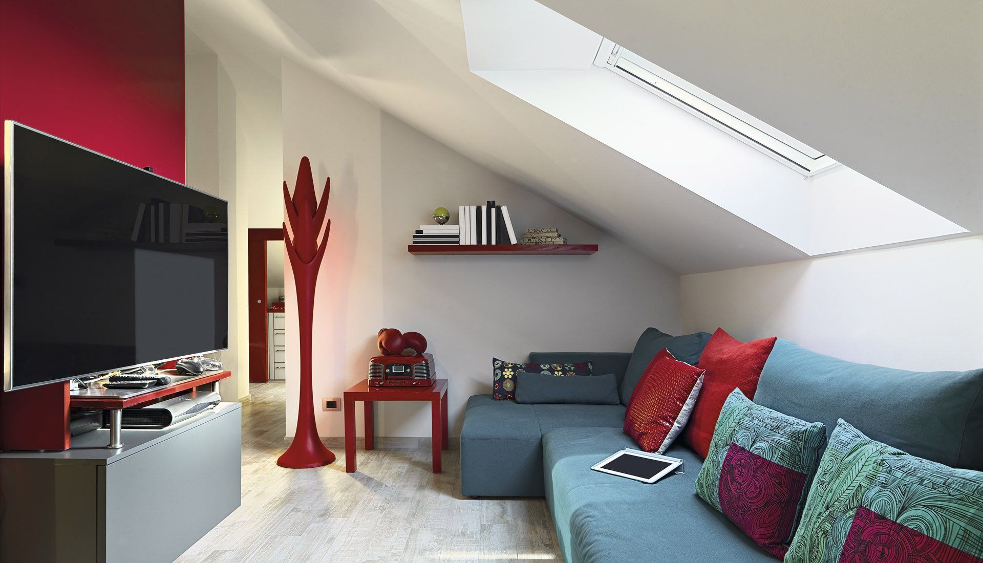 A cozy attic living room with a blue sectional sofa, red accents, a TV, and a skylight.