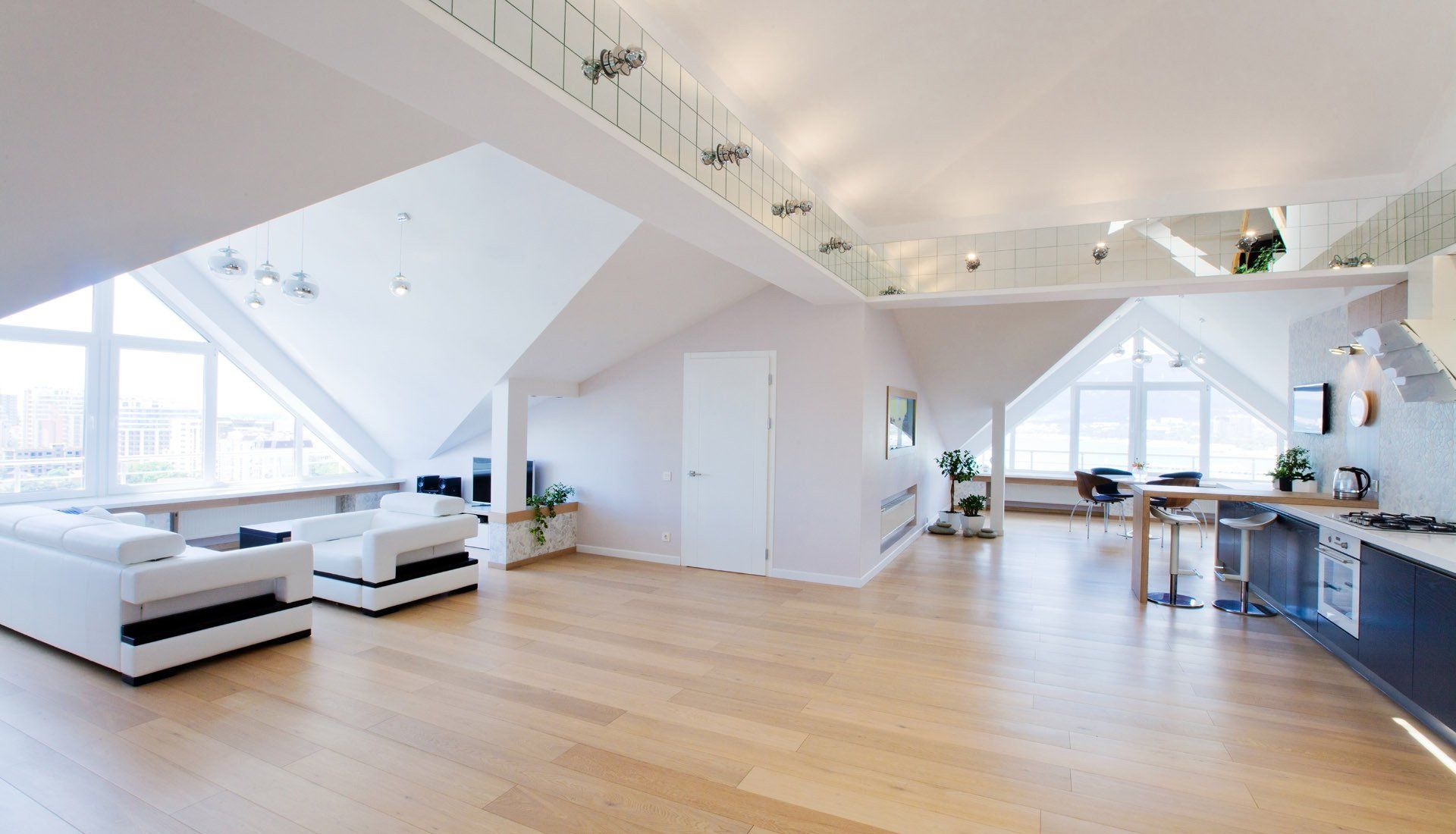 A bright, modern open-plan attic apartment with white furniture, wooden floors, and a kitchen area under a sloped ceiling.