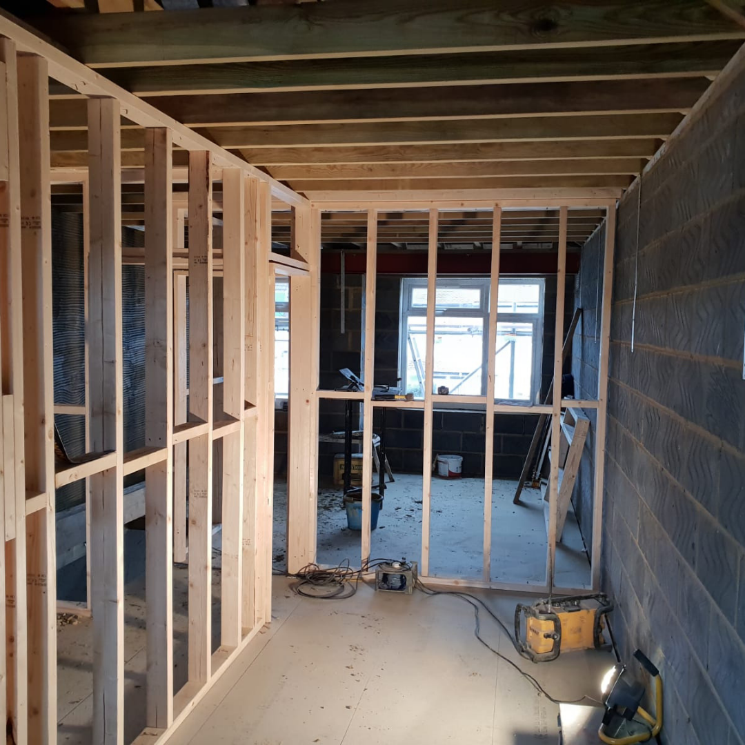 Interior construction site featuring unfinished wood wall framing, exposed ceiling joists, and a concrete block wall.