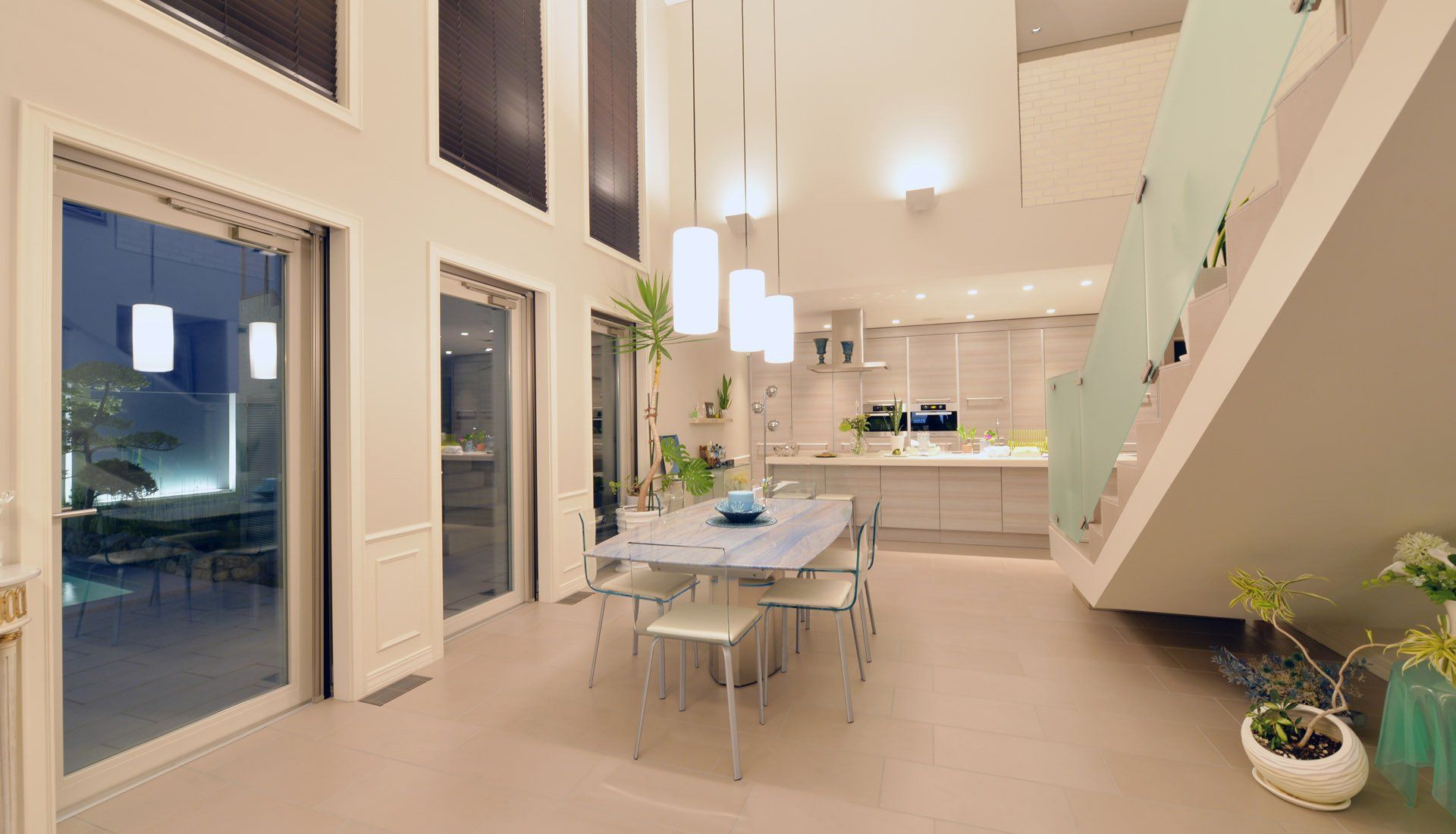 Modern open-concept dining room with high ceilings, tall windows, and a staircase leading to an upper floor.