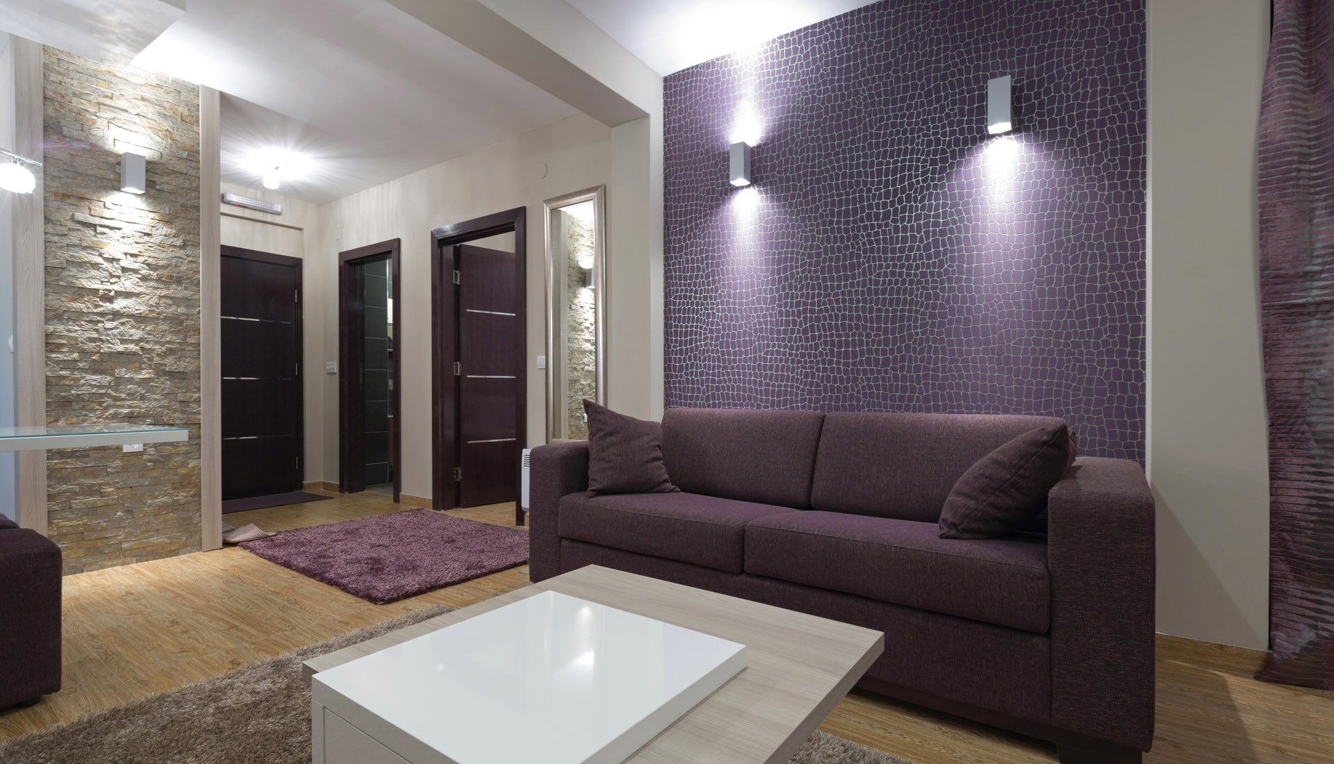 A living room with a purple sofa, patterned wall, stone accent pillar, and a white coffee table.