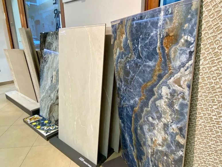 Grandi lastre decorative in pietra esposte in posizione verticale in uno showroom, tra cui piastrelle grigio-blu e color crema.