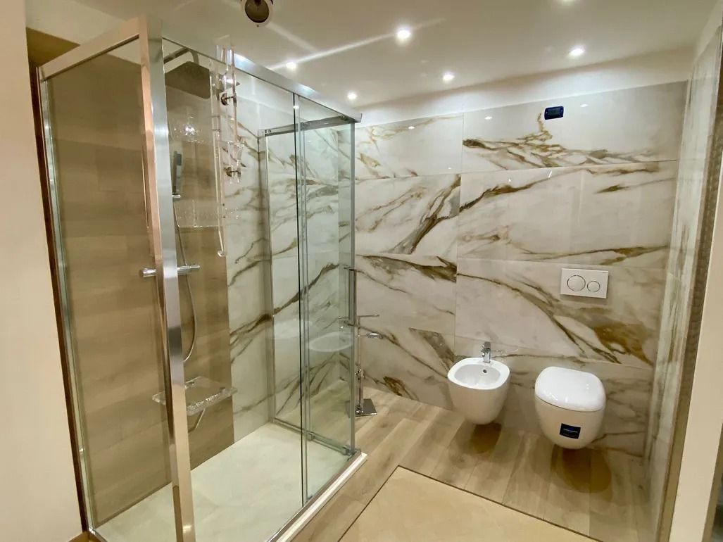 Bagno moderno con doccia in vetro, pareti in marmo e WC e bidet sospesi.