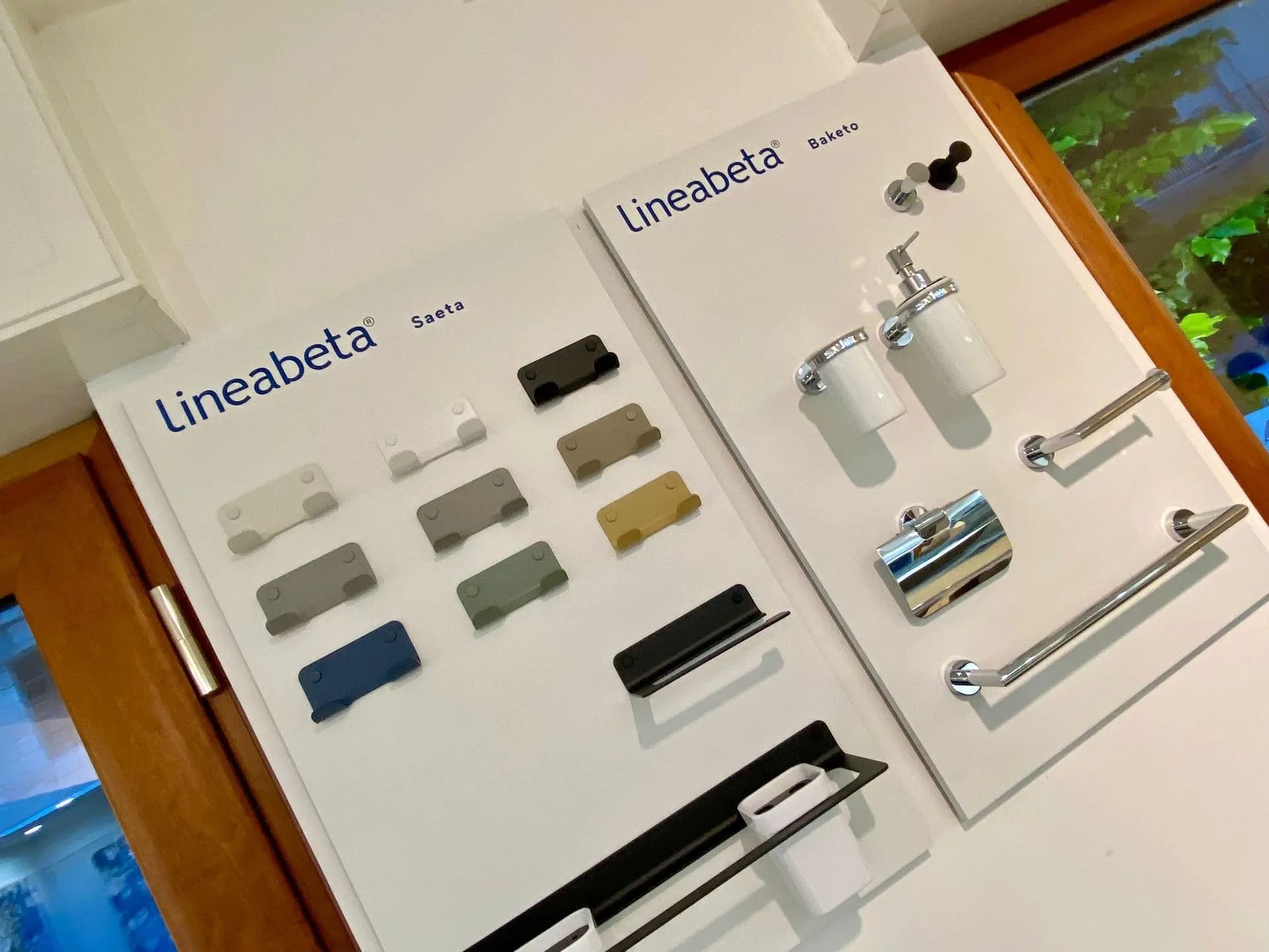 Esposizione di accessori per il bagno con rubinetti, maniglie e portasciugamani su pannelli bianchi.
