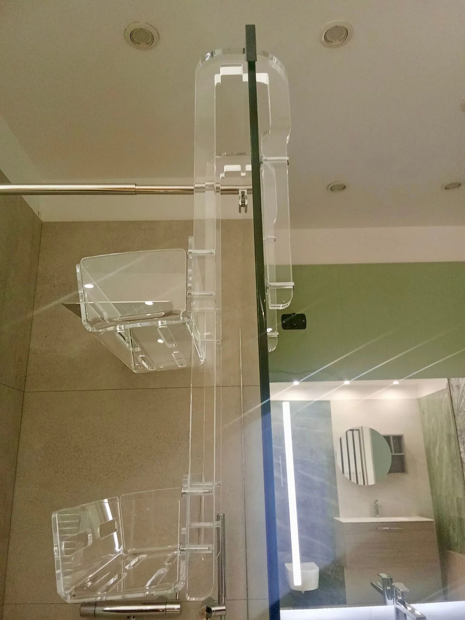 Mensole a parete in acrilico trasparente in un moderno spazio interno, con specchio e luci del soffitto riflessi nelle vicinanze.