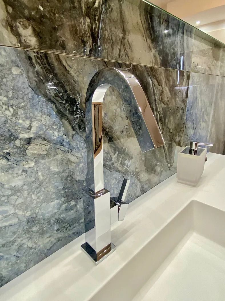 Rubinetto da bagno moderno cromato su un rivestimento in marmo grigio sopra un lavabo bianco.