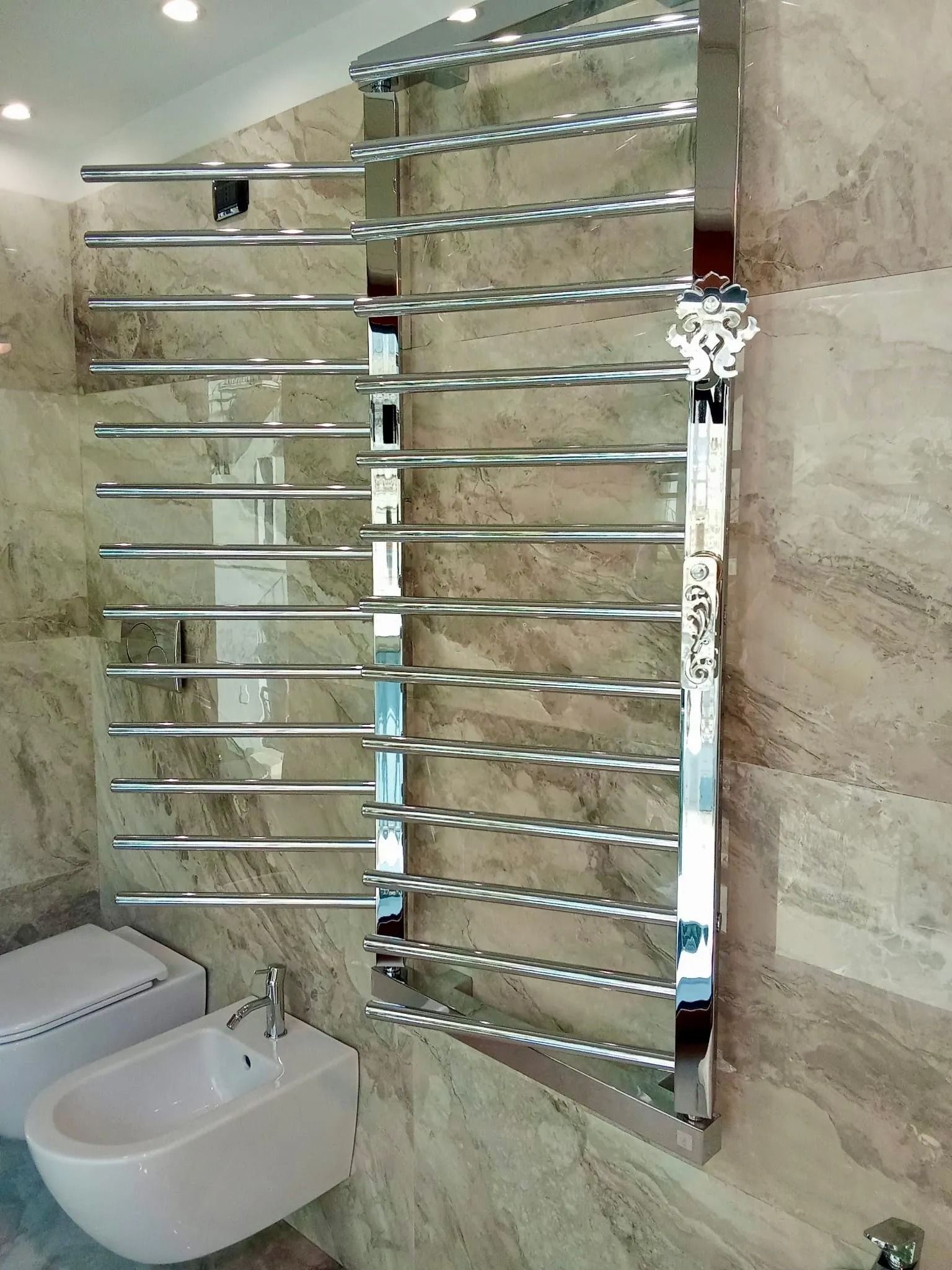 Bagno moderno con scaldasalviette cromato sopra un lavabo bianco a parete e piastrelle in pietra beige.
