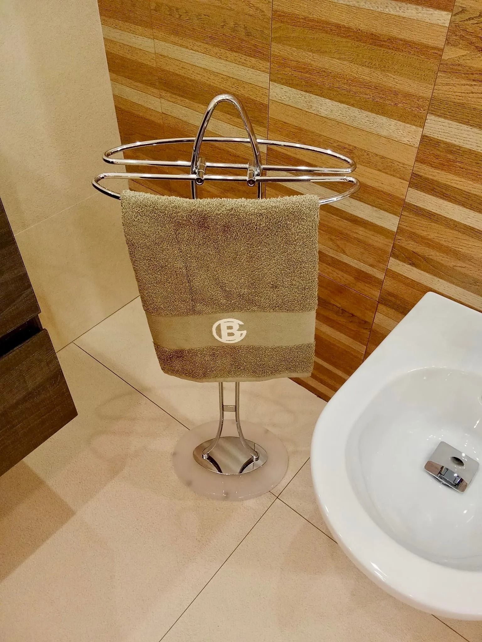 Un asciugamano appeso a un supporto cromato accanto a un lavandino bianco e a una parete rivestita in legno in un bagno.