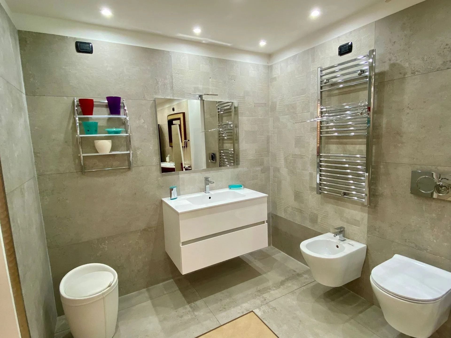 Bagno moderno con piastrelle beige, doppio lavabo, bidet, WC, scaldasalviette e specchio a parete.